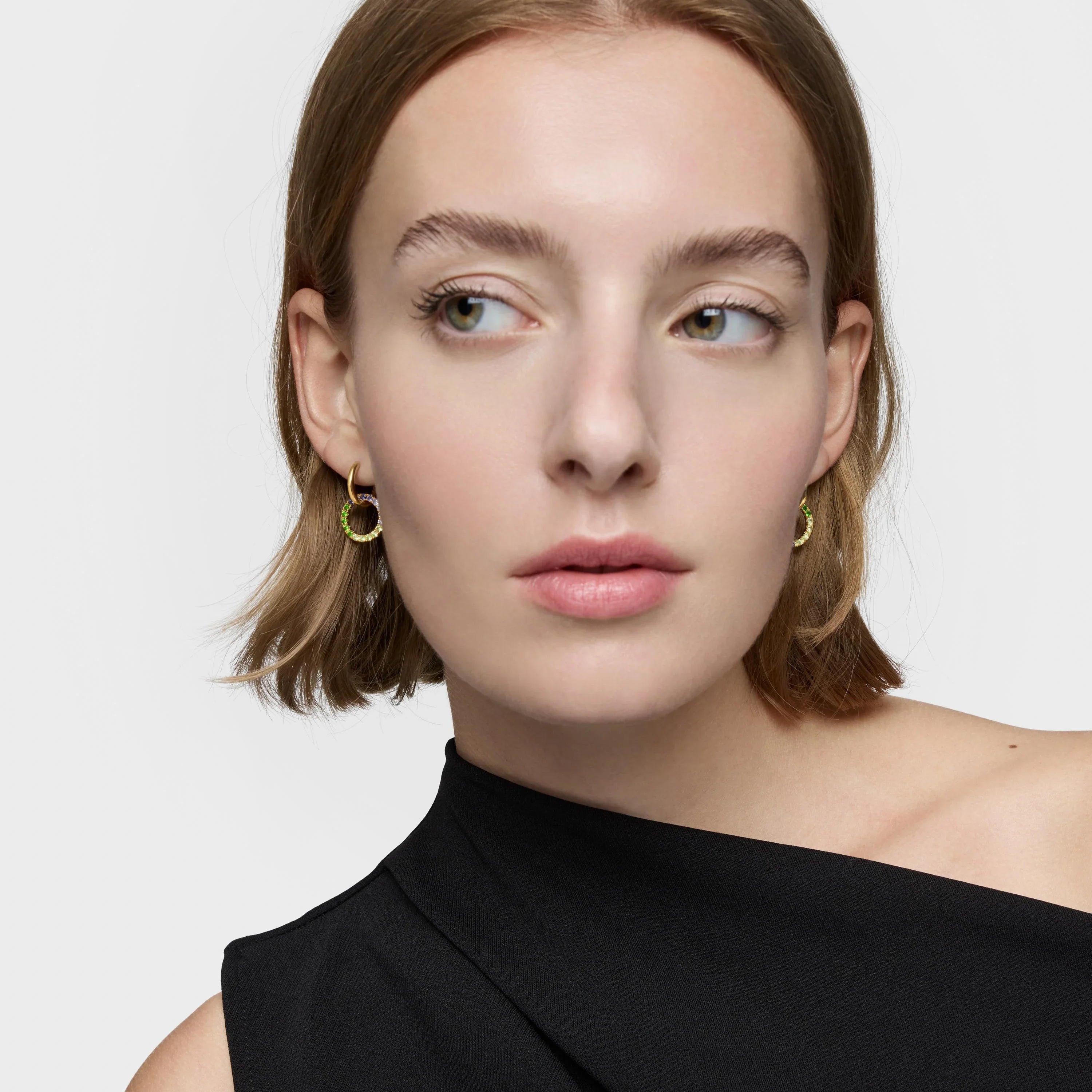 אישה עם שיער בלונדיני קצר, עונדת עגילי חישוק זהב, לובשת שמלה שחורה אלגנטית