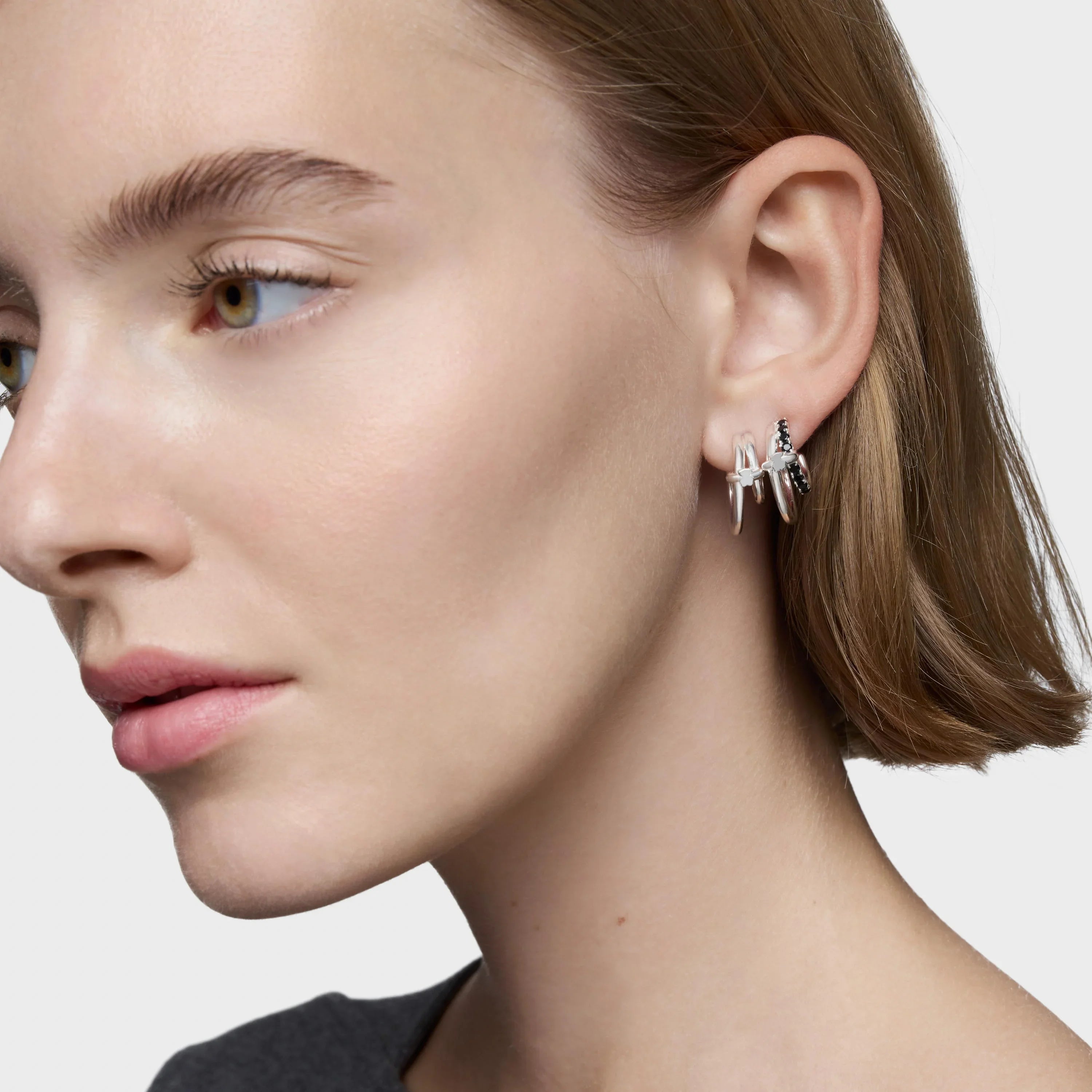 אישה עונדת עגילים כסופים עם עיטורי קוצים ועיצוב ייחודי על אוזן, תקריב על הפנים