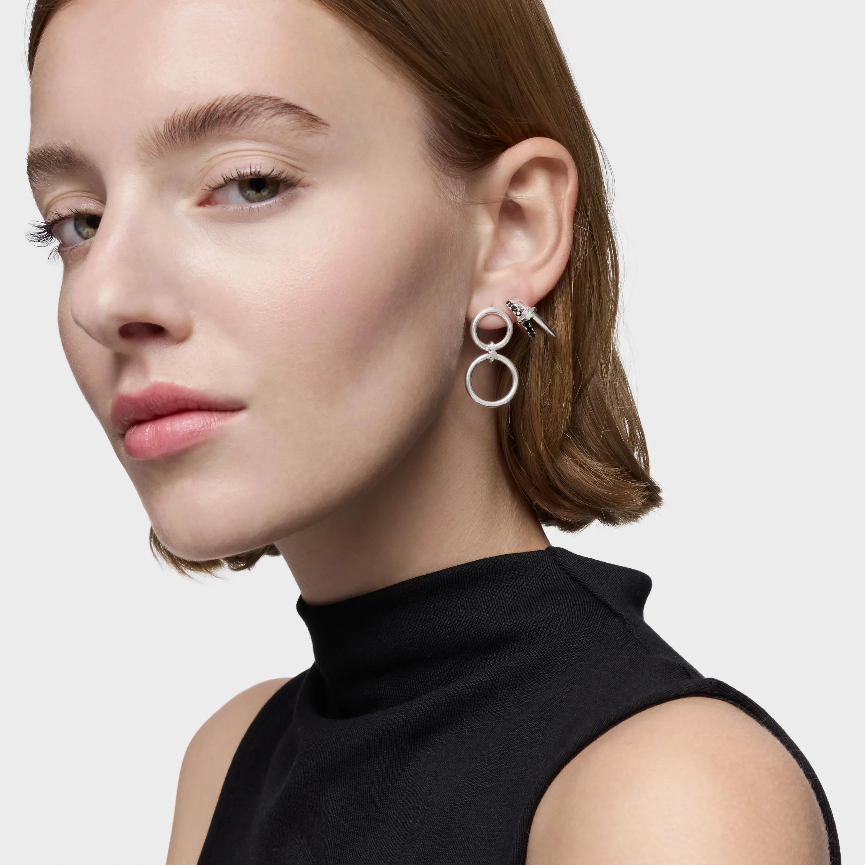 אישה עונדת עגילי חישוק כפולים מכסף, חולצת גולף שחורה, רקע בהיר