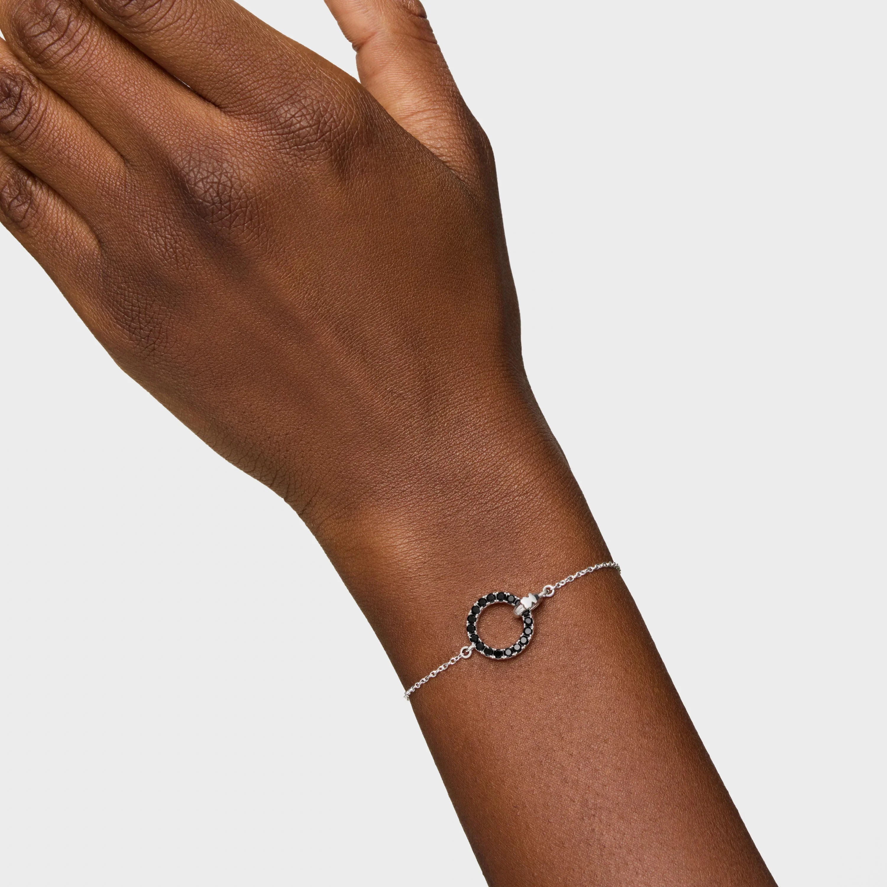 צמיד כסף עדין עם תליון עגול משובץ אבנים שחורות על יד של דוגמנית