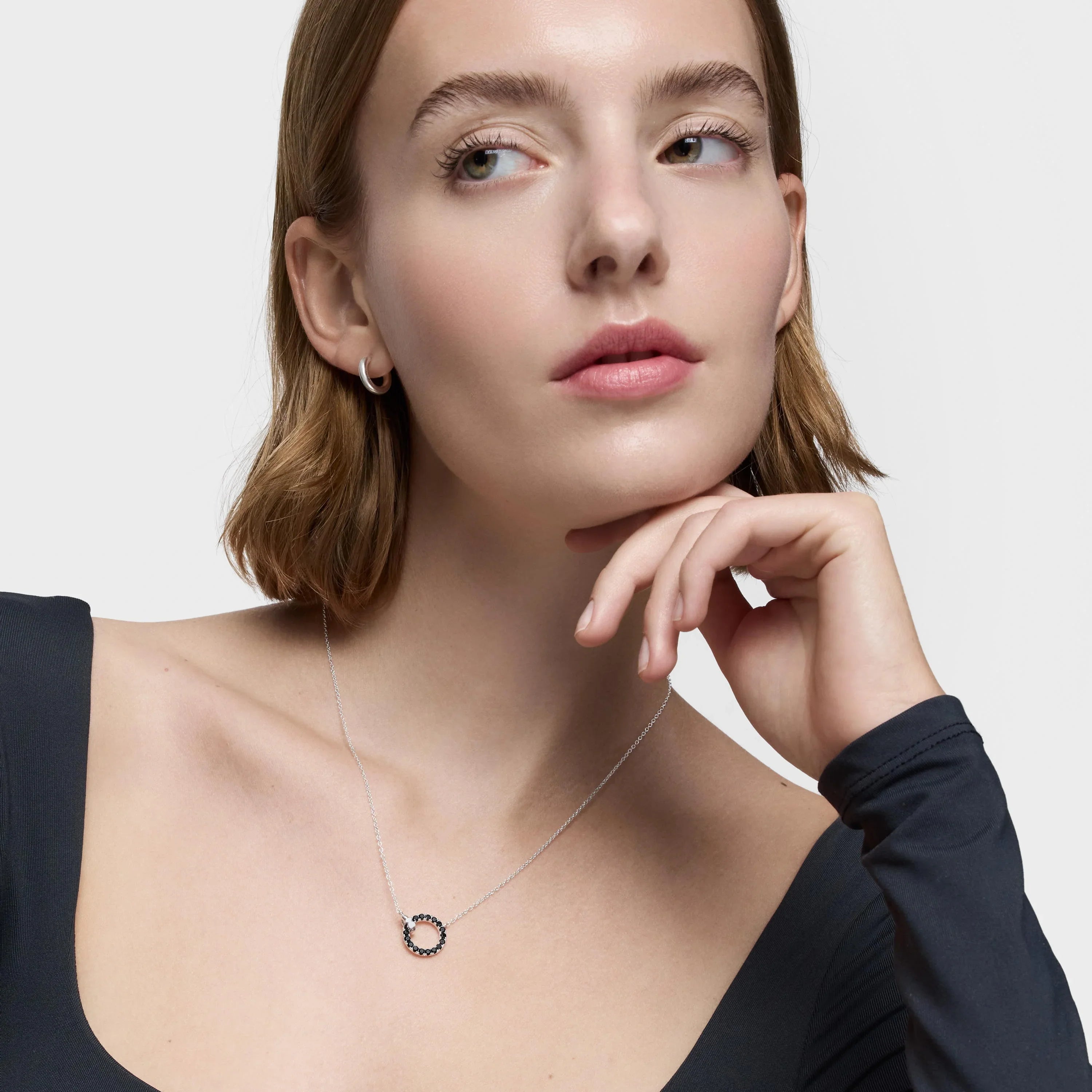 דוגמנית עונדת שרשרת כסף עדינה עם תליון עגול, רקע בהיר, תכשיטים אופנתיים לנשים