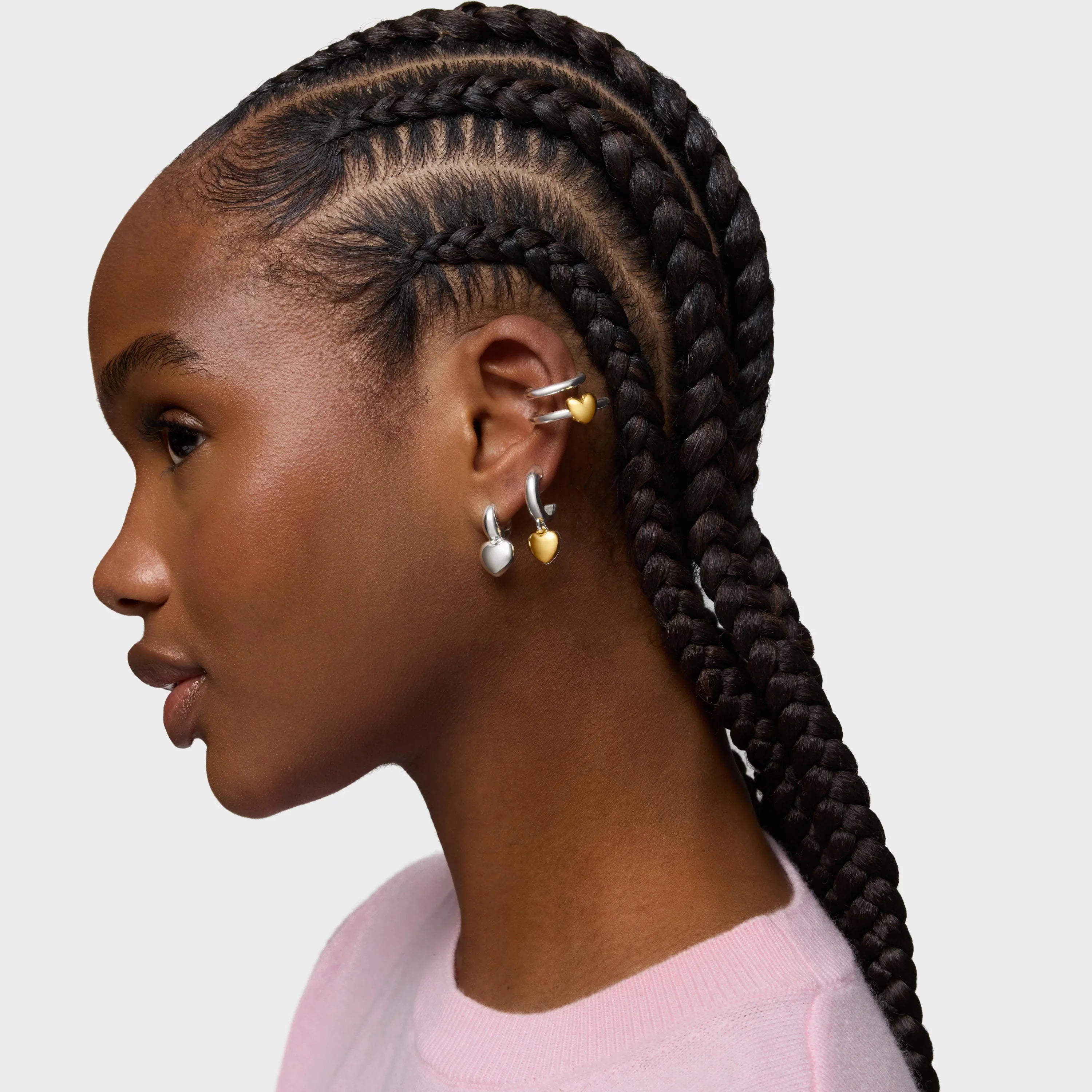 אישה עם צמות בוקס בריידס ועגילי חישוק בצורת לב זהב וכסף, חולצת סווטשירט ורודה