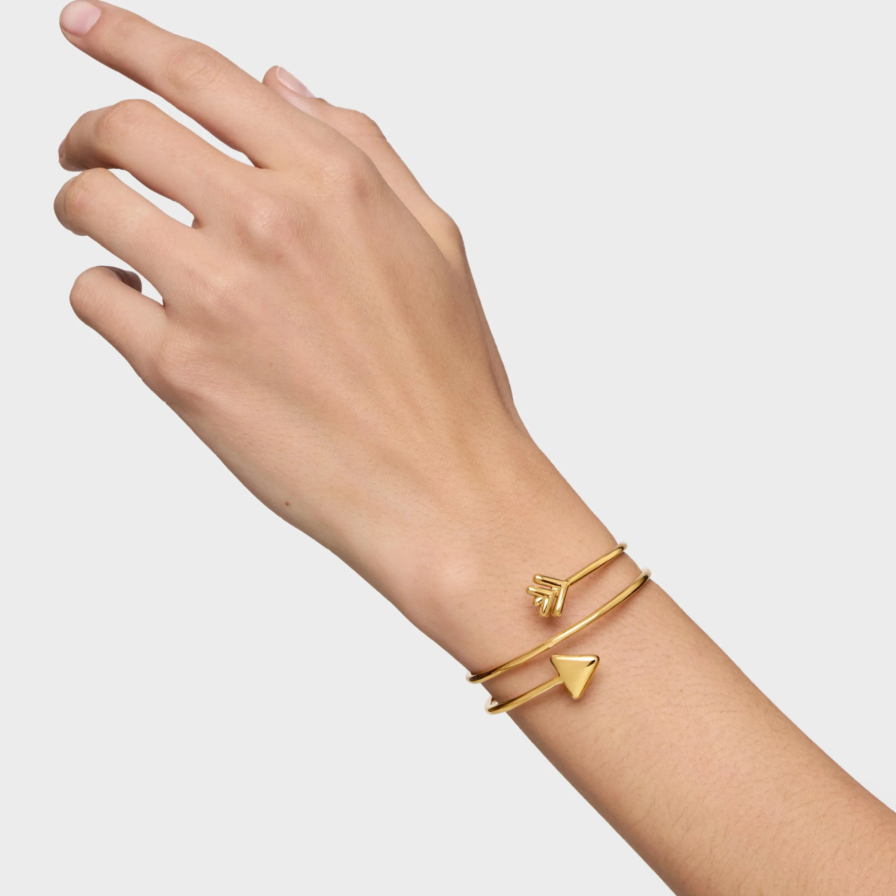צמיד פתוח מזהב בעיצוב חץ משולש על פרק כף יד של אישה רקע לבן