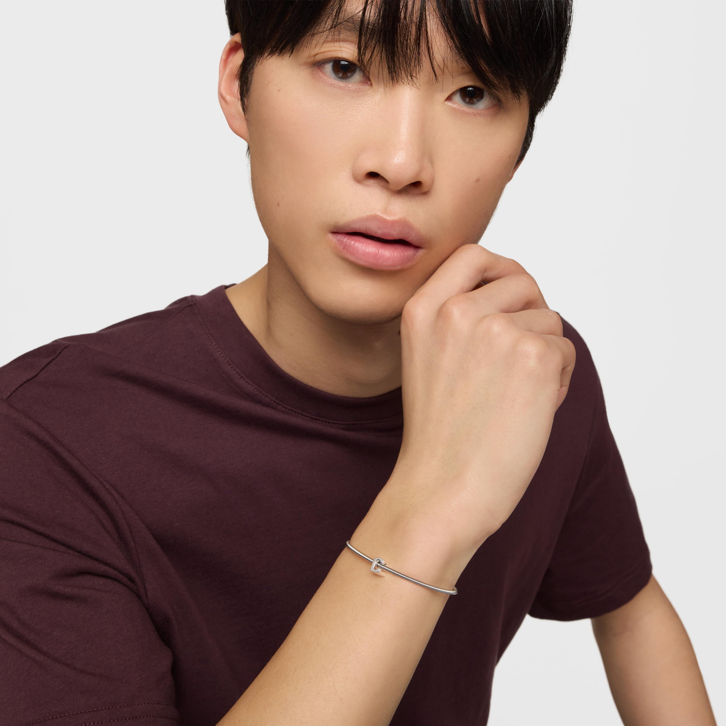 גבר עם צמיד כסף דק על היד, לובש חולצה סגולה, רקע לבן