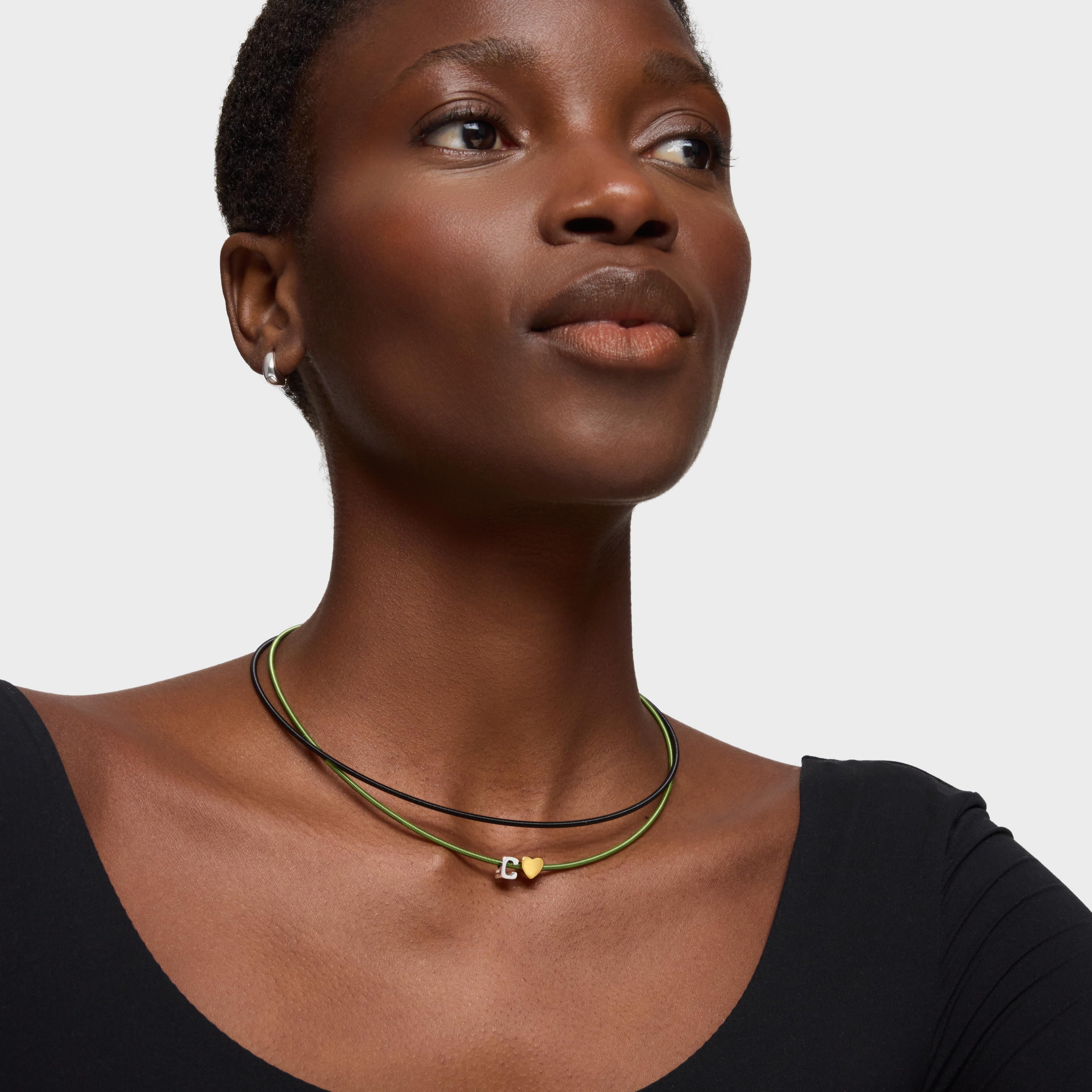 אישה עונדת שרשרת כפולה עם תליון לב זהב על רקע לבן, תכשיטי אופנה מודרניים