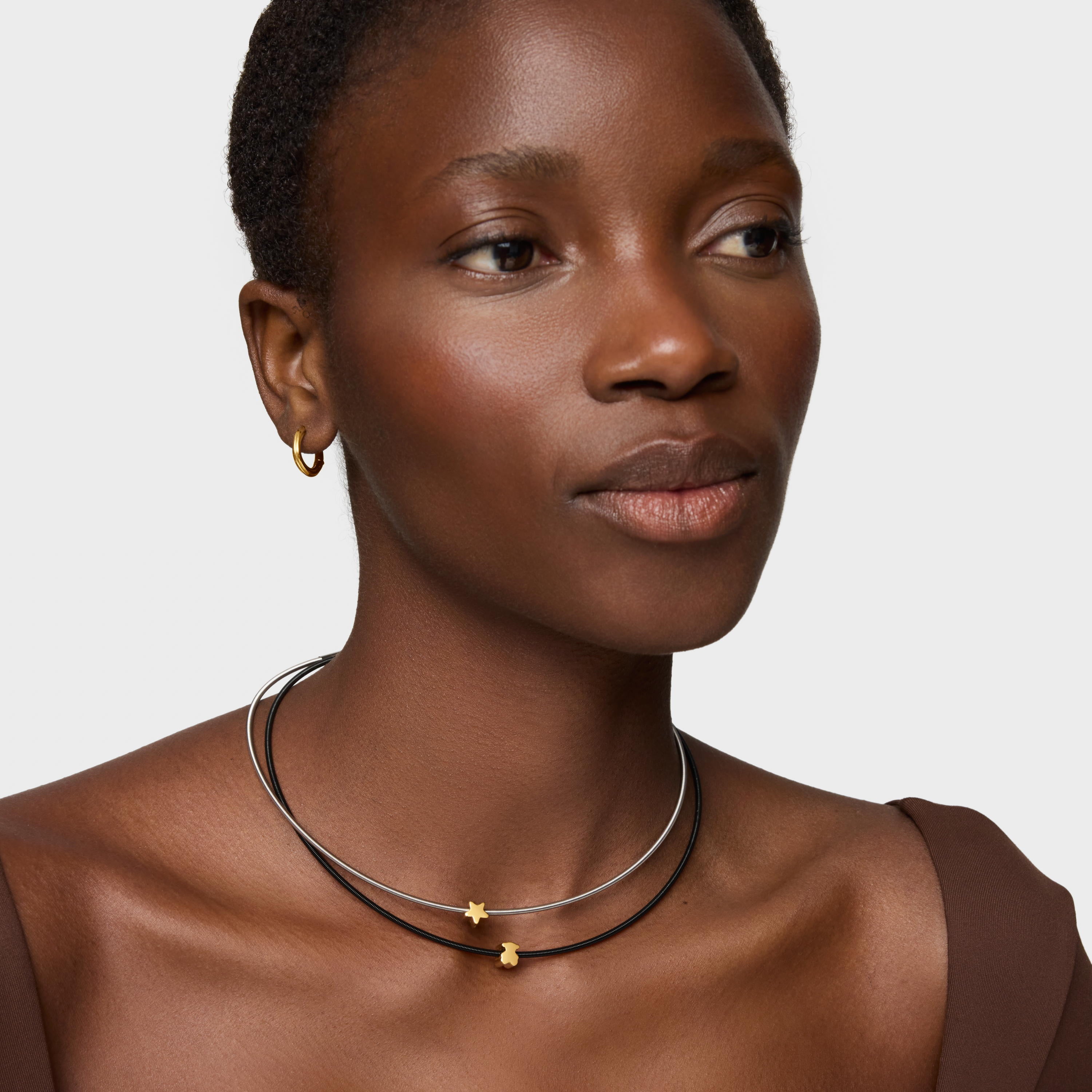 אישה עונדת שרשרת דו-שכבתית עם תליונים בגוון זהב ועגיל חישוק קטן, אופנה מודרנית