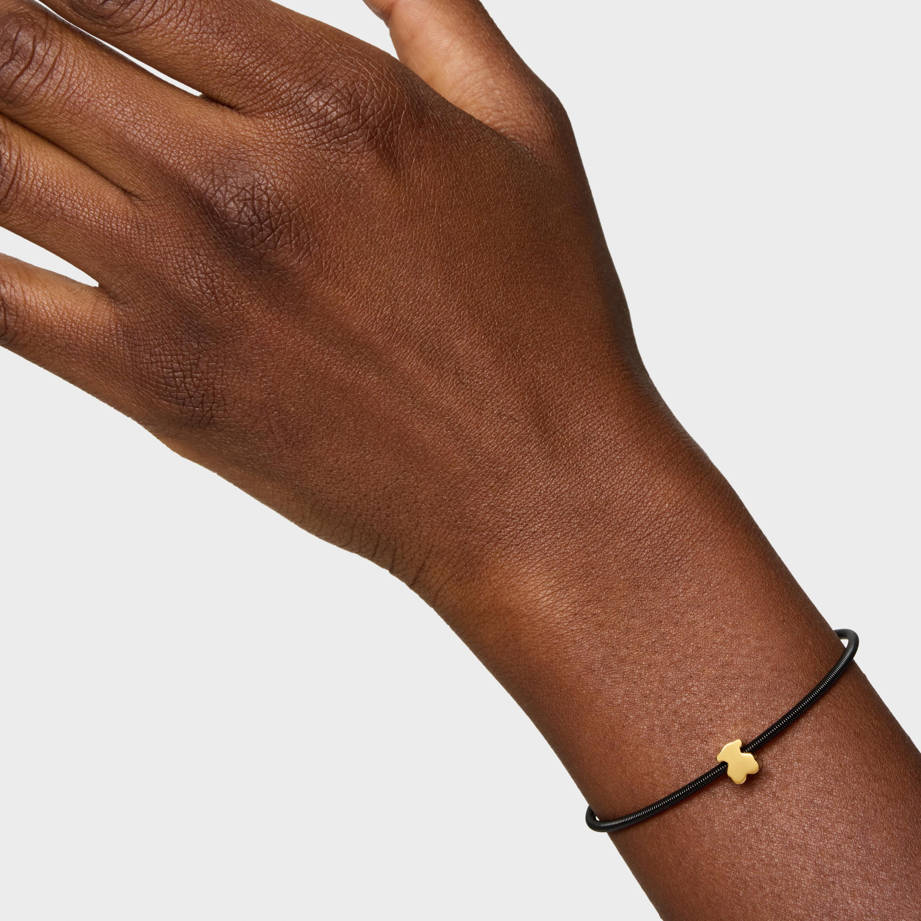 יד עם צמיד עדין, חוט שחור ותליון זהב קטן בצורת דובי, על רקע לבן