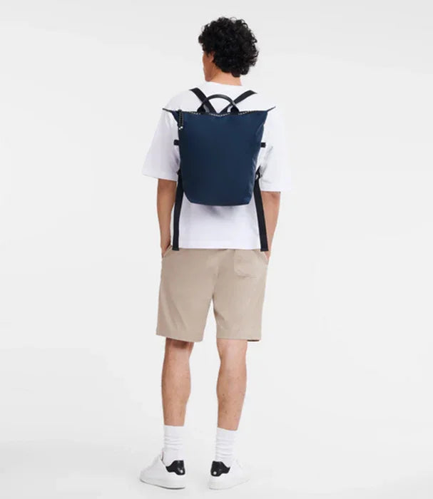 גבר לובש תיק גב כחול, חולצה לבנה ומכנסי שורט בז׳, צילום מוצר לאופנה ב-CHOZEN מותגים מובילים