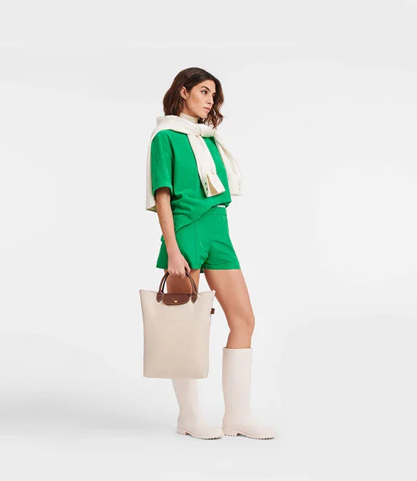 אישה בלבוש ירוק, מגפיים לבנים ותיק בעמידה, מותג אופנה CHOZEN