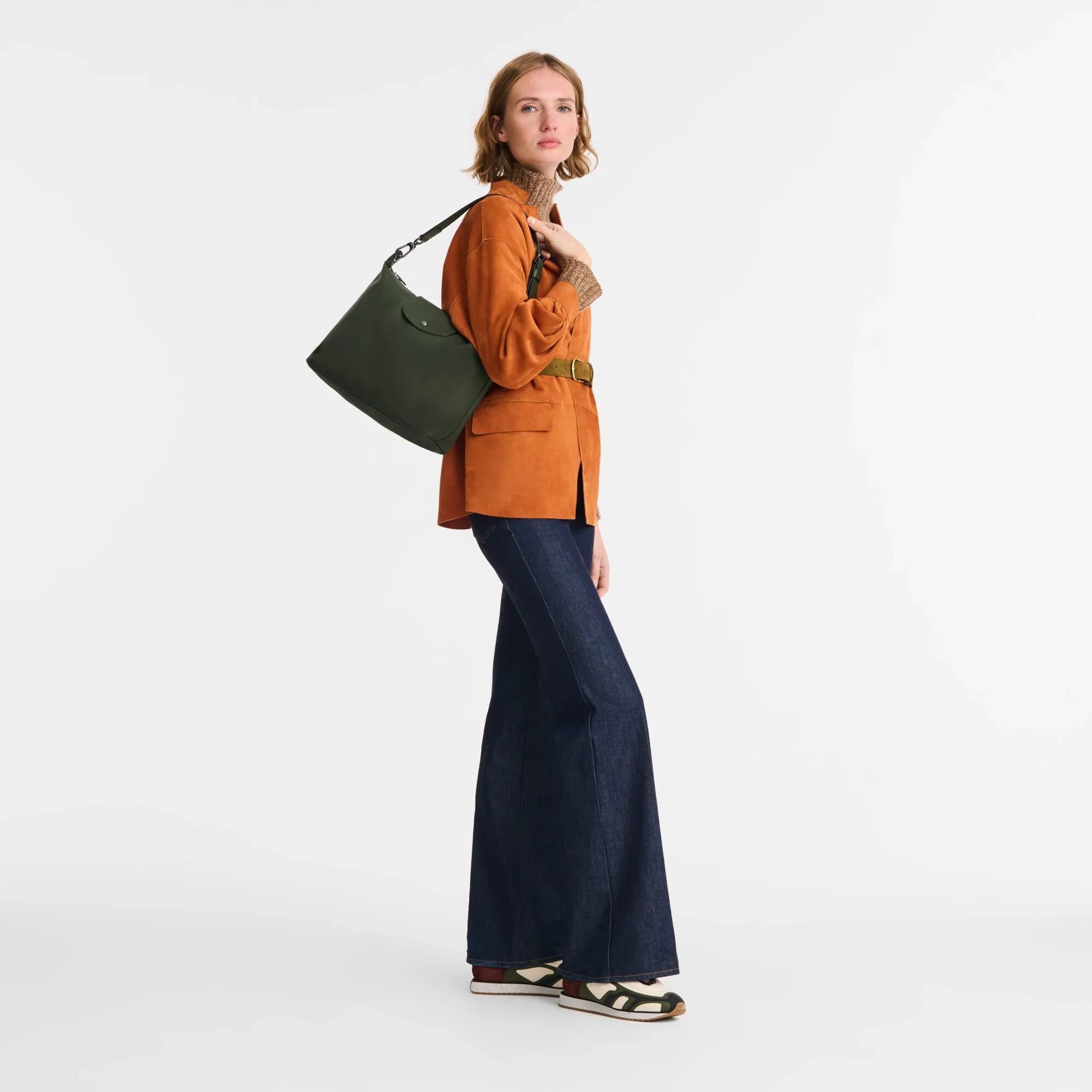 דוגמנית עם תיק ירוק אופנתי, ז'קט כתום ומכנסי ג׳ינס רחבים, CHOZEN מותגים מובילים