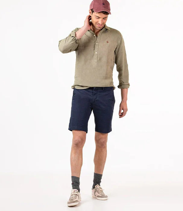 דגם גבר לובש חולצה ירוקה עם כפתורים, מכנסיים קצרים כחולים, כובע אדום ונעלי סניקרס CHOZEN