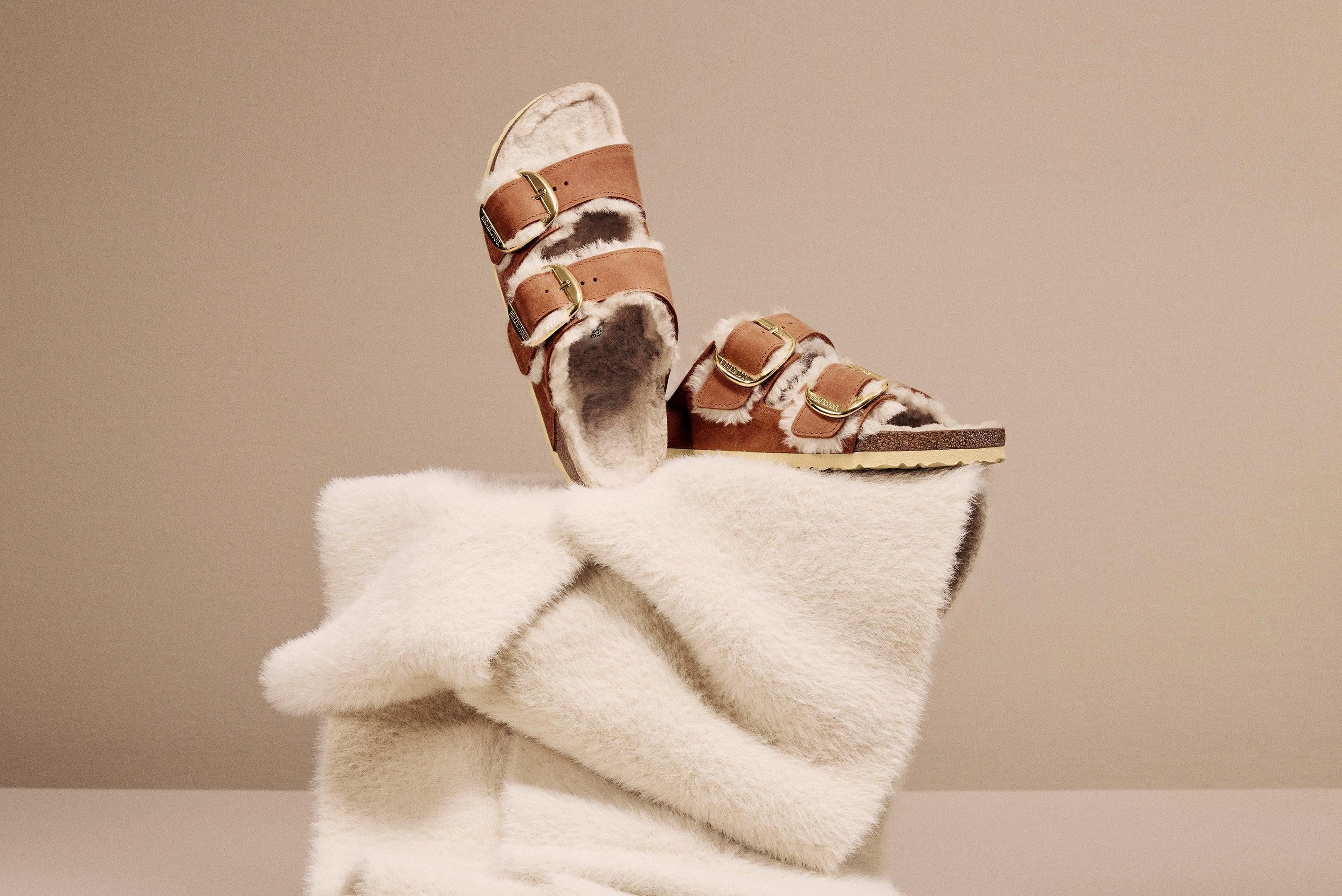 סנדלי עור חום עם פרווה פנימית ושני אבזמים, מונחים על בד קטיפתי, מבית CHOZEN קבוצת אלפא