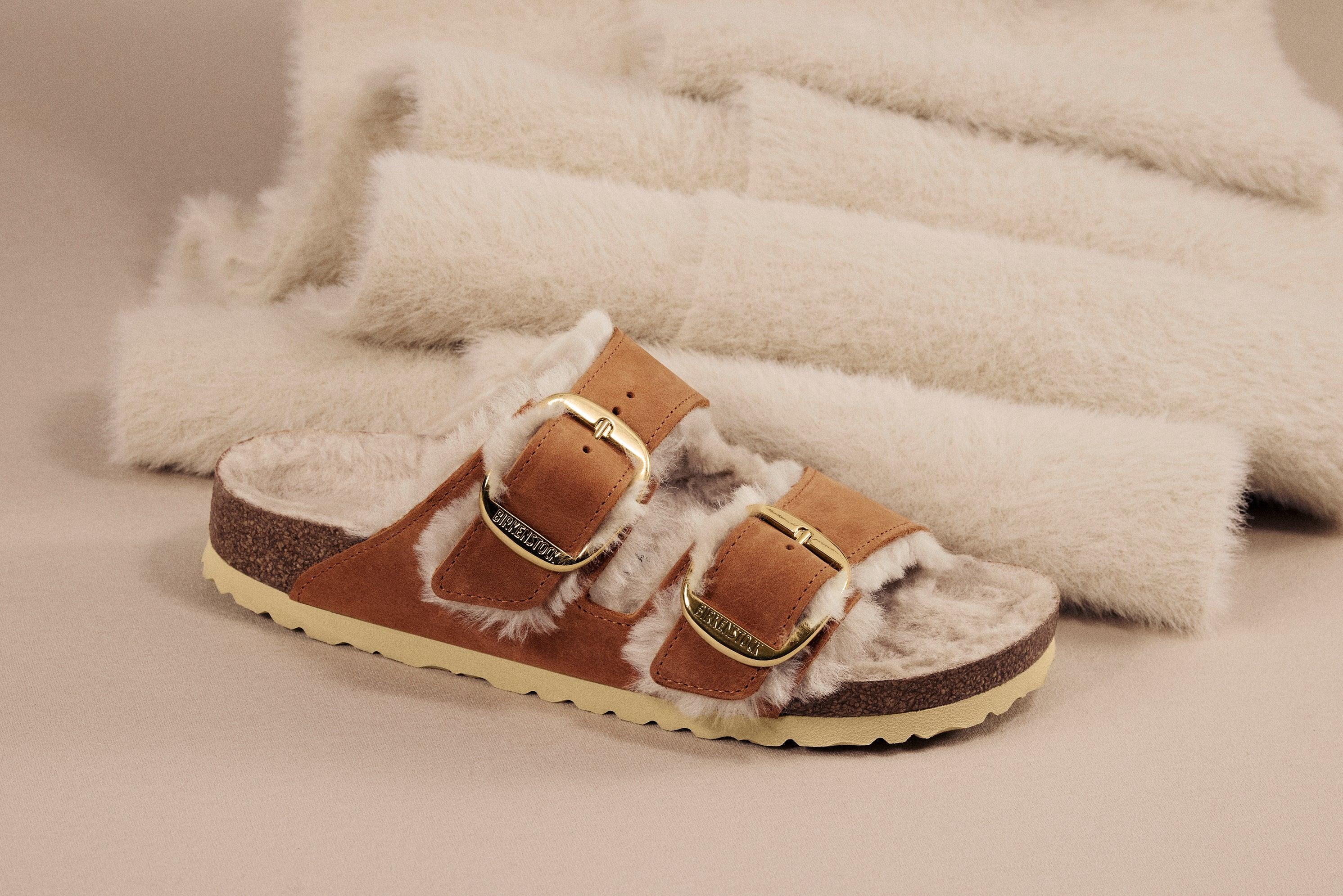 כפכף בריקנשטוק עם פרווה בצבע בז', אבזמים מוזהבים, מוצג על רקע טקסטיל רך, CHOZEN