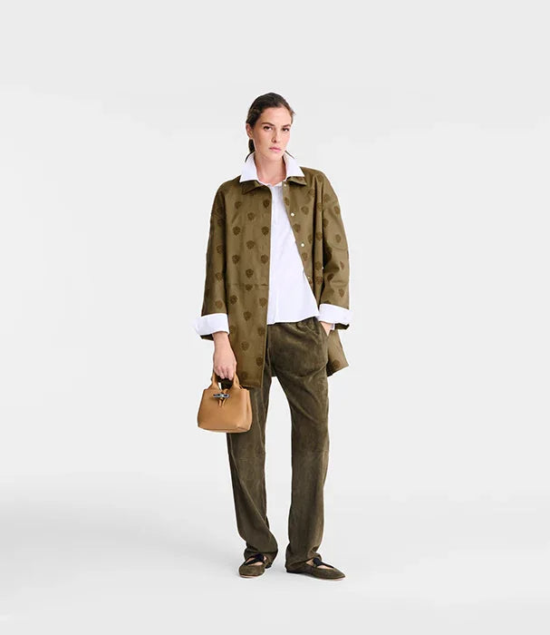 אישה לובשת ז’קט ירוק עם דוגמא, חולצה לבנה ומכנסיים תואמים, מחזיקה תיק חום, אופנה CHOZEN