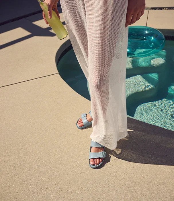 אישה עם כפכפים אופנתיים ותחתית רשת לבנה עומדת ליד בריכה, מחזיקה בקבוק ליד, CHOZEN