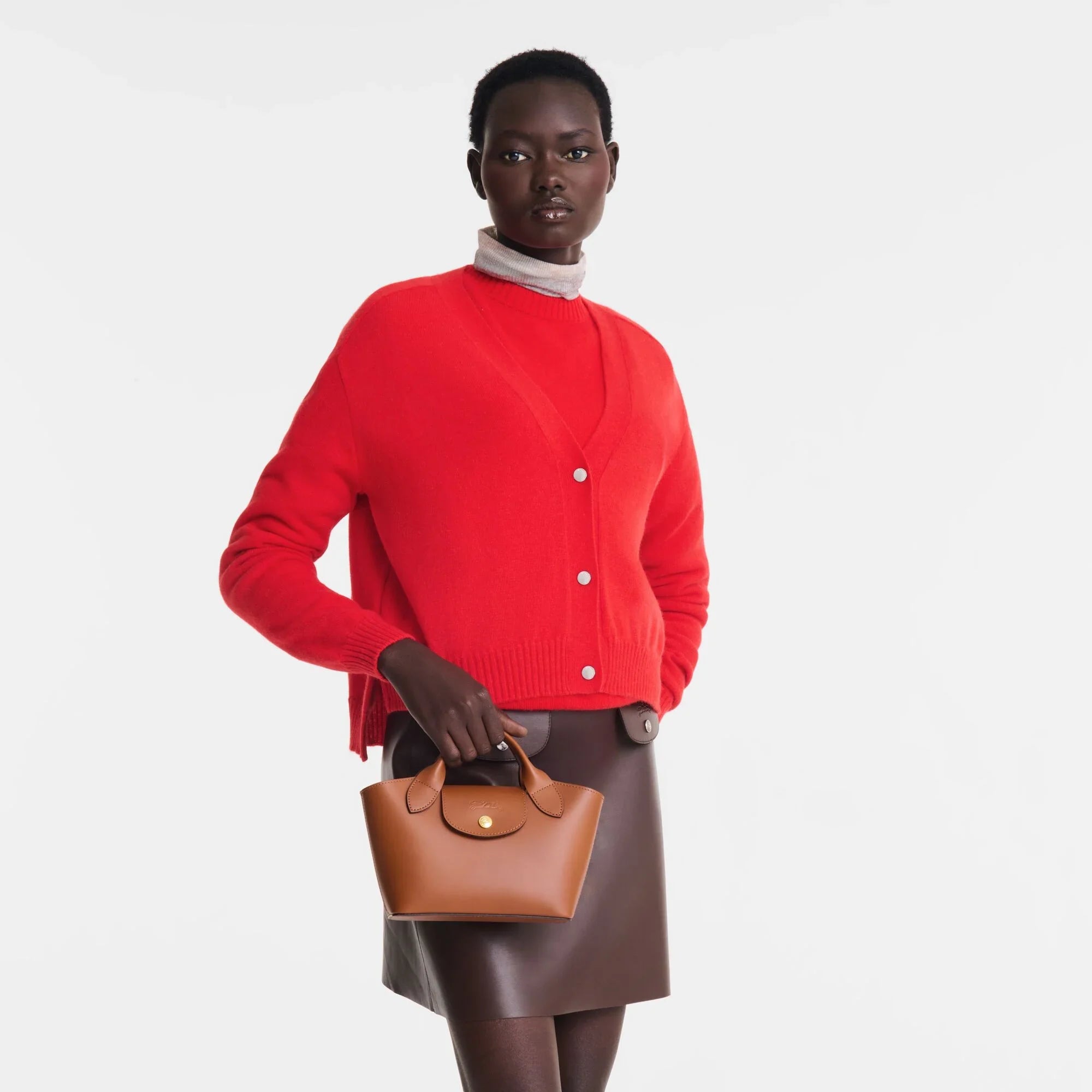 דוגמנית לובשת סוודר אדום וחצאית חומה, מחזיקה תיק עור חום, אופנה יוקרתית מבית CHOZEN