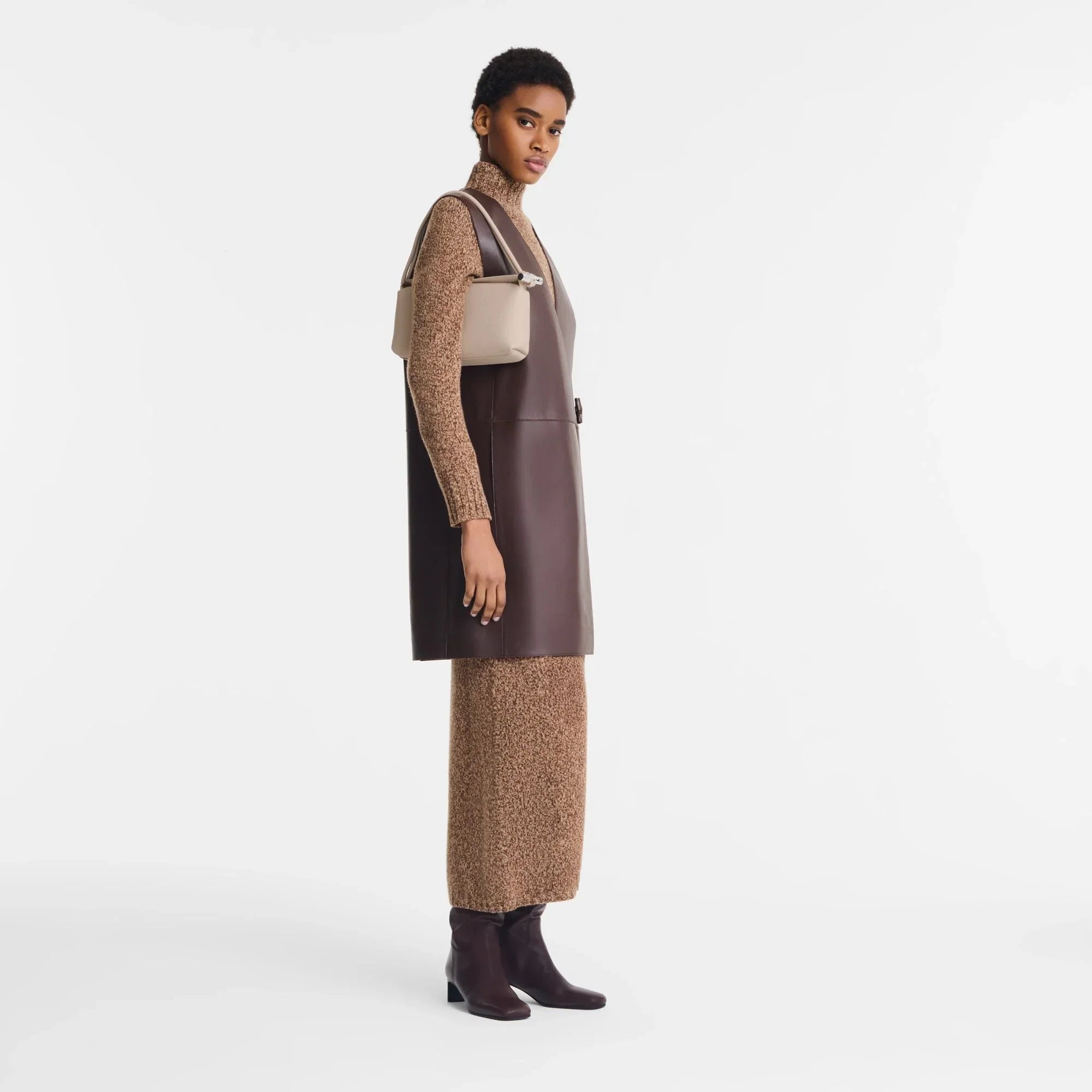 דוגמנית לובשת שמלת מקסי חומה עם וסט עור כהה, מגפיים ותיק אופנתי, אופנת CHOZEN