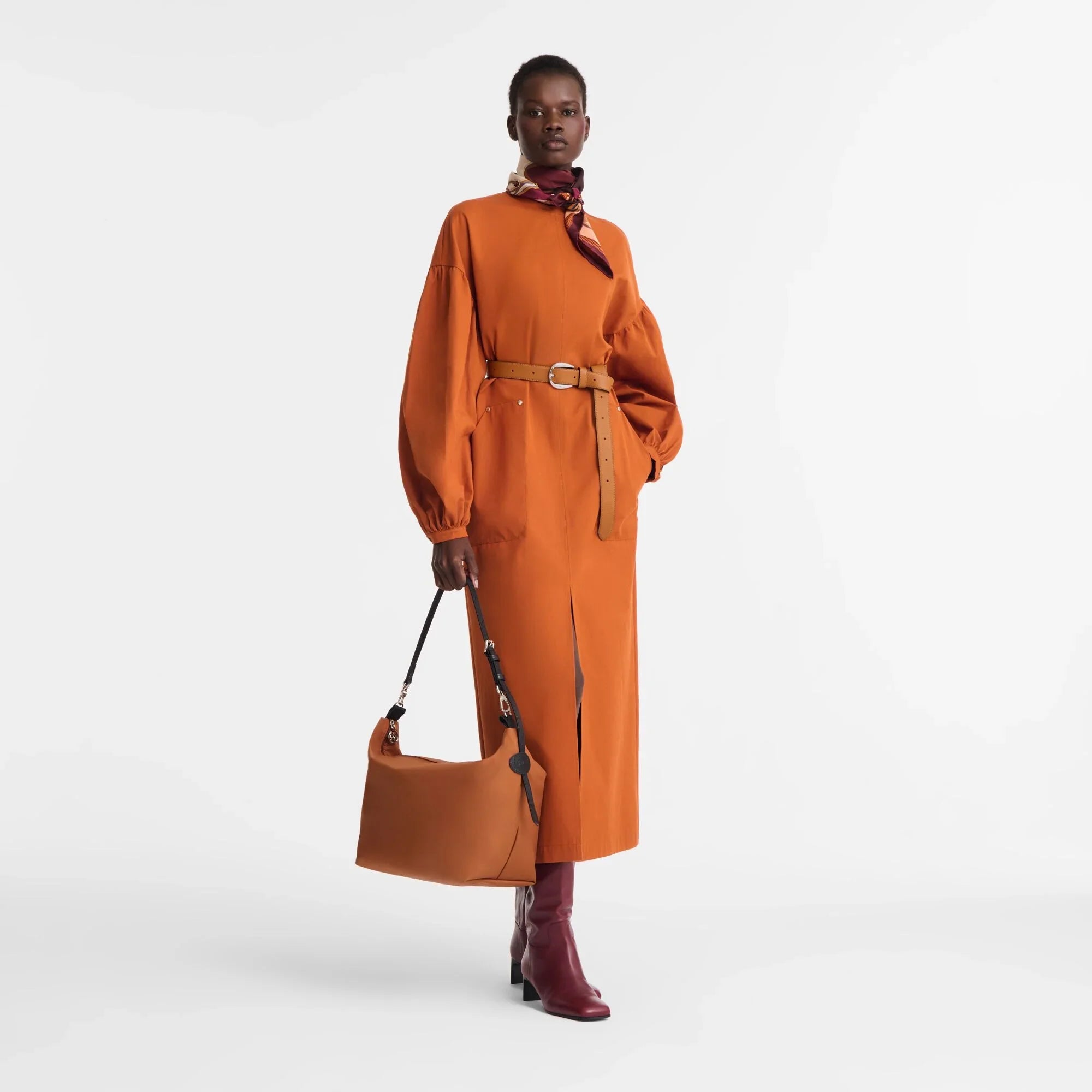 אישה לובשת שמלה כתומה אופנתית עם חגורה, מגפיים חומים ותיק תואם, צילום אופנה מבית CHOZEN