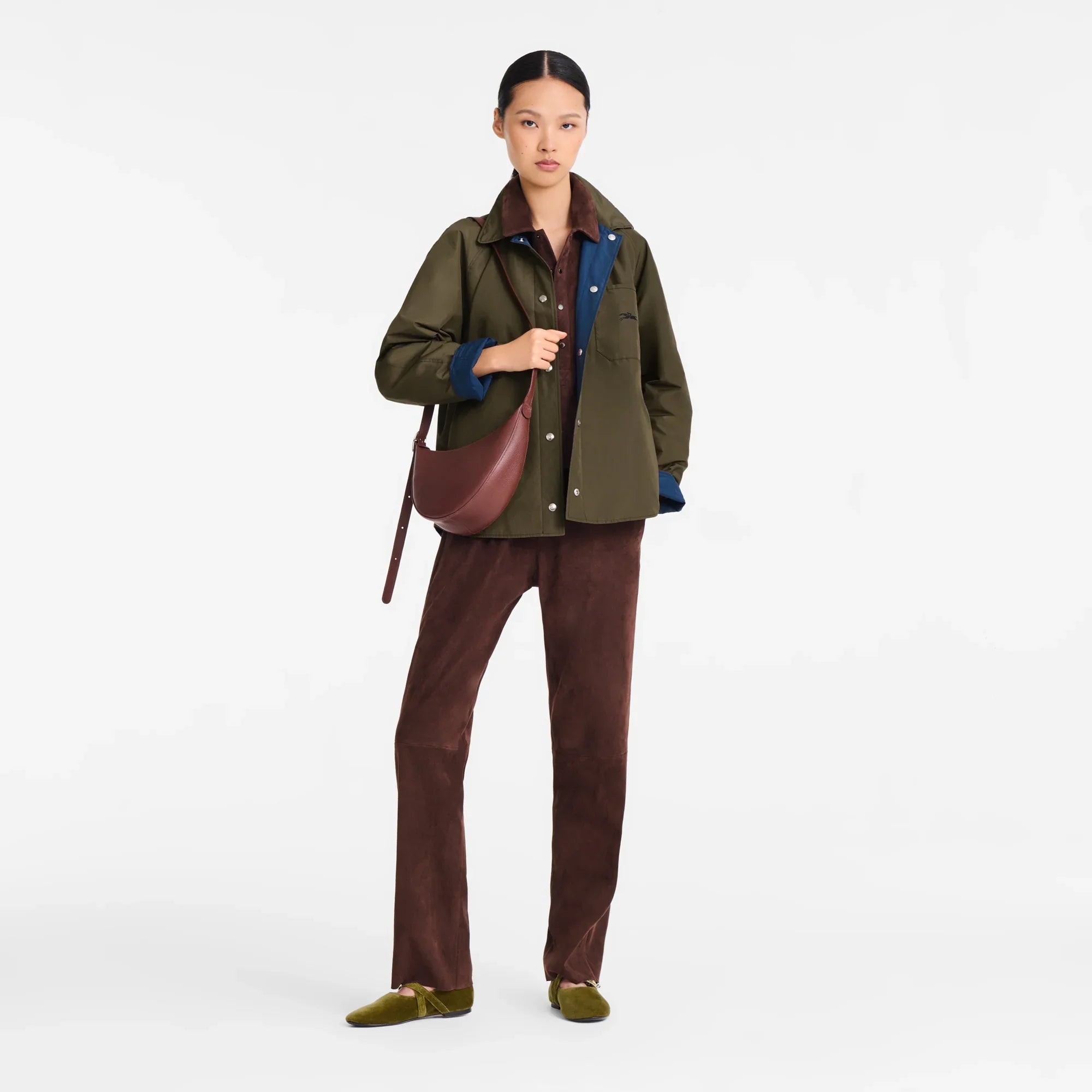 אישה לובשת מעיל ירוק, מכנסיים חומים ונעלי מוקסין, עם תיק חום ב-CHOZEN