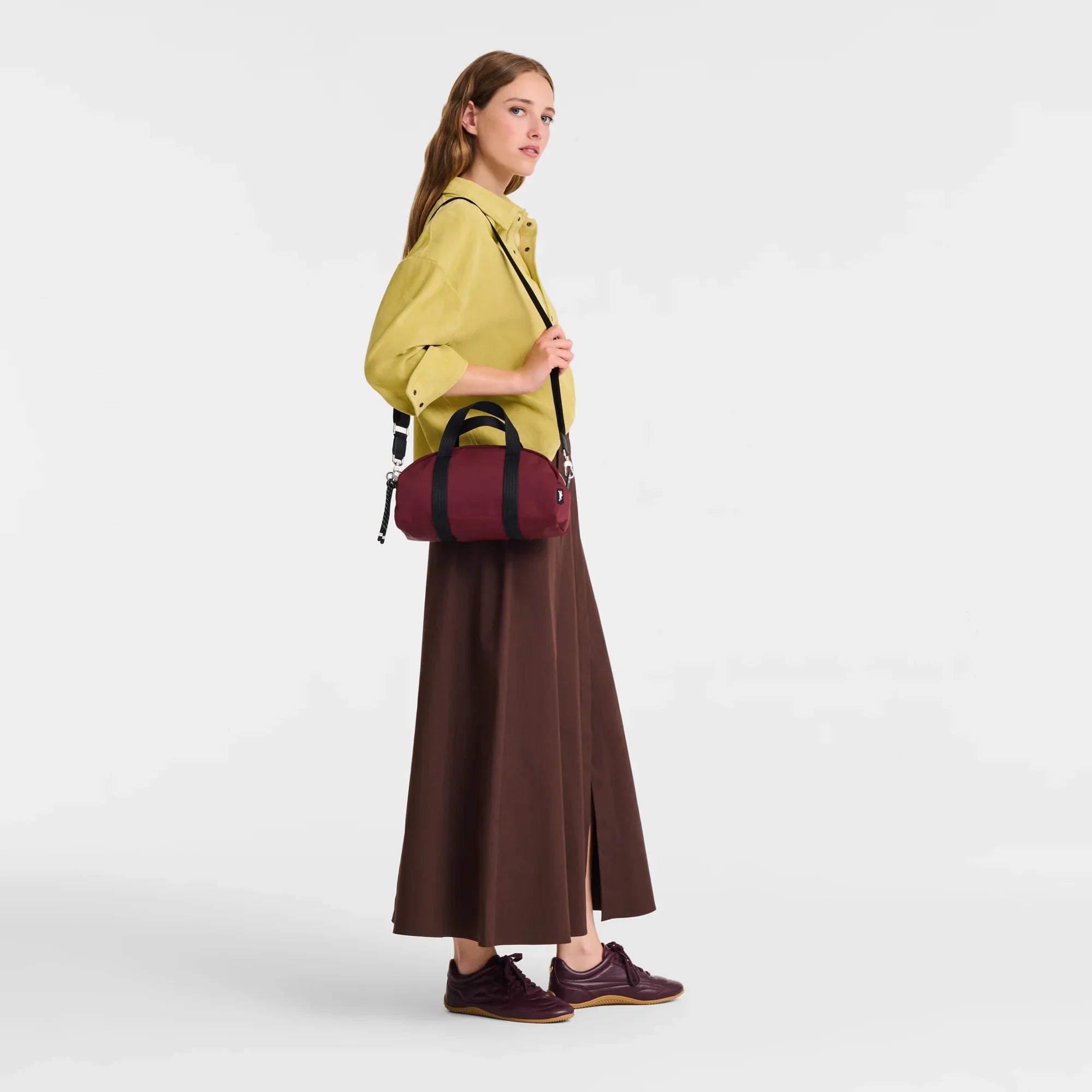 אישה עם תיק צד קטן בצבע בורדו, לוק אופנתי של CHOZEN, חולצת חרדל וחצאית חומה ארוכה