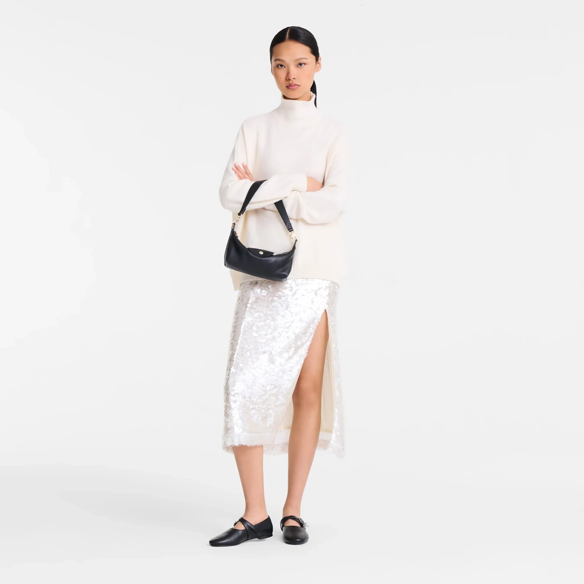 אישה עם סוודר לבן, חצאית פאייטים כסופה עם שסע, תיק עור שחור ונעליים שחורות, אופנה CHOZEN