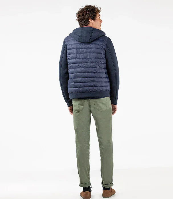 גבר לובש מעיל פוך כחול כהה עם קפוצ'ון, מכנסיים ירוקים ונעליים חומות, צילום סטודיו ל-CHOZEN