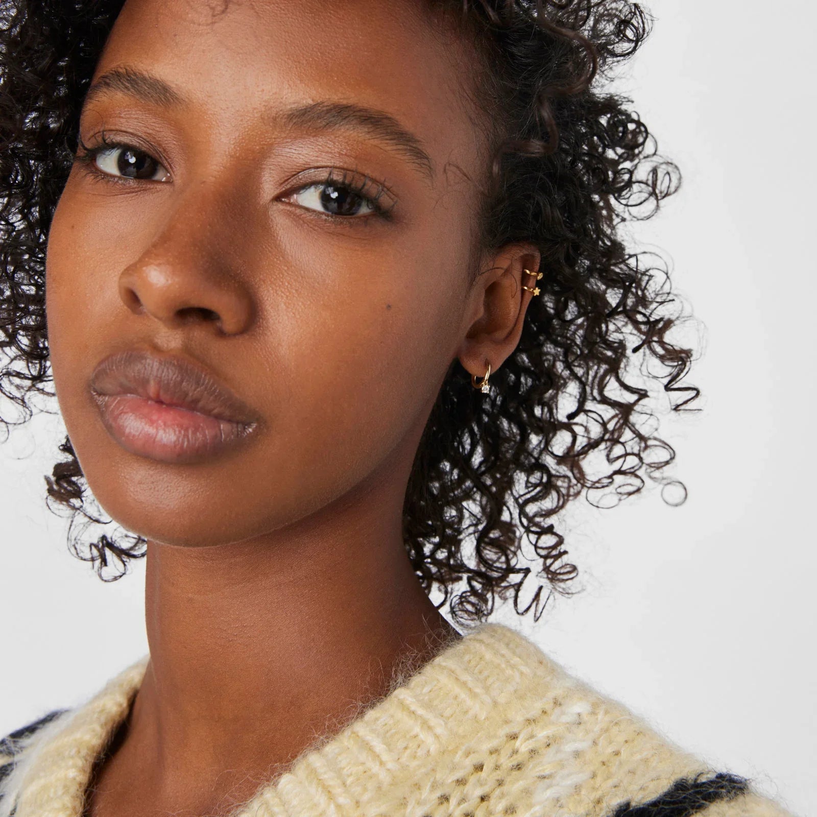 תקריב על אישה עם עגילים עדינים מזהב, שיער מתולתל, חולצת סריג, קולקציית CHOZEN