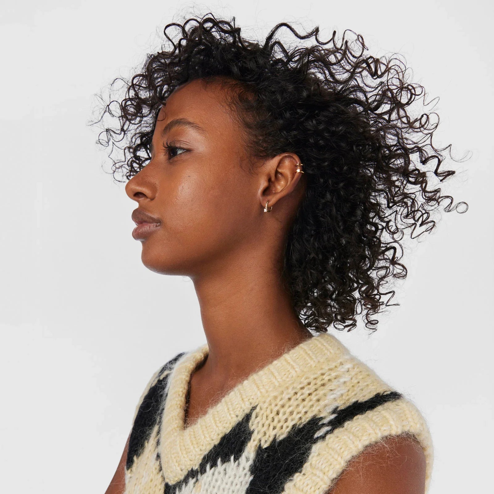 דוגמנית עם שיער מתולתל ועגילים מוזהבים, לובשת סוודר צהוב שחור, CHOZEN אופנה טרנדית