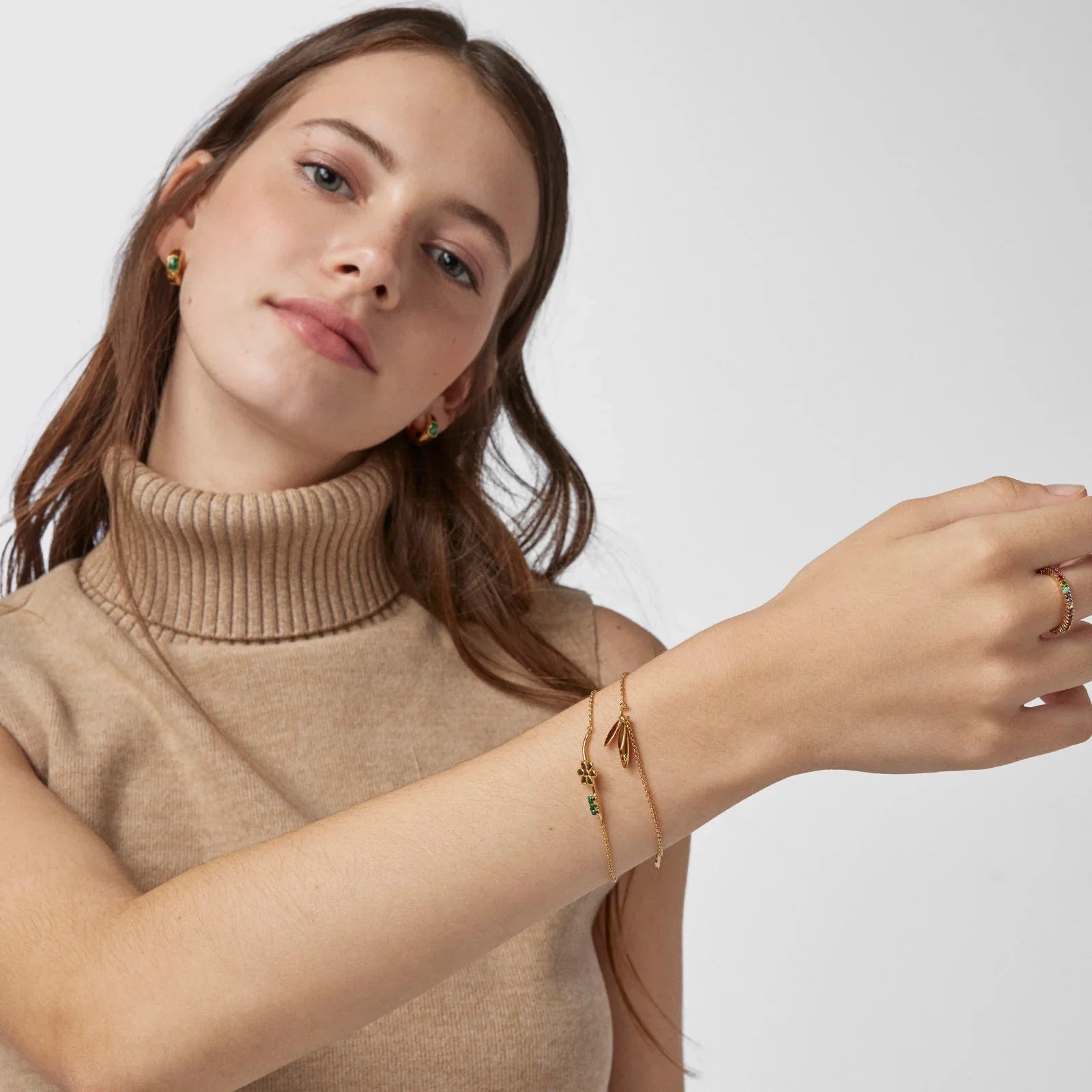 אישה עם סוודר בז', עונדת תכשיטי זהב על פרק היד והאצבע, עגילים בעיצוב מעודן, CHOZEN