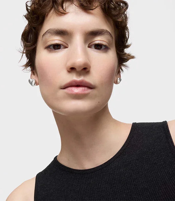 אישה עם שיער קצר עונדת עגילי כסף מעוצבים, לובשת גופיה שחורה, צילום תקריב מאתר CHOZEN