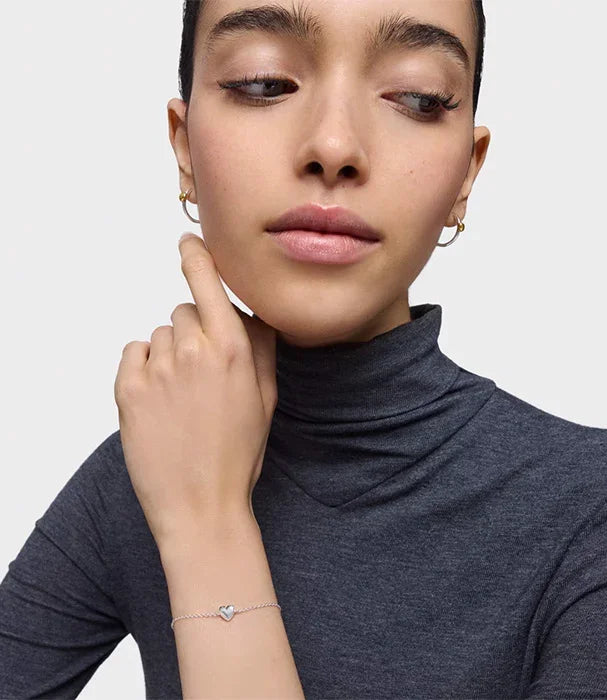 אישה עונדת עגילים זהב וצמיד עדין עם תליון לב, צילום תכשיטים CHOZEN