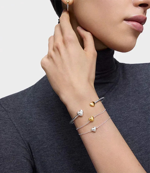 אישה עם חולצת גולף כהה עונדת צמידים ועגיל זהב בצורה לב, תכשיטי CHOZEN מבית קבוצת אלפא