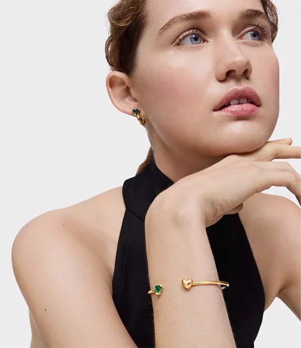 אישה עונדת עגילי זהב וירוק וצמיד זהב עם לב, צילום אופנה CHOZEN מותגים מובילים