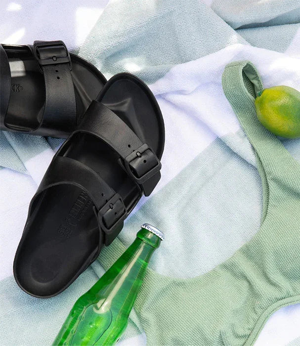 כפכפי בריקנשטוק שחורים לצד מגבת, בקבוק ירוק ולימון, CHOZEN מותגים מובילים