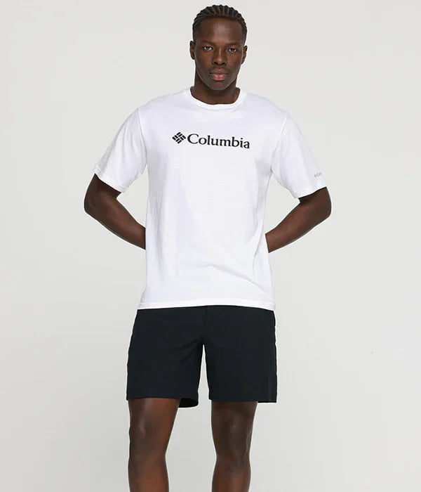 דגם עומד בחולצת קולומביה לבנה ומכנסיים קצרים שחורים, אופנת גברים מותג Columbia