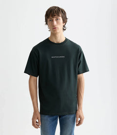 דוגמן לובש חולצת טי שחורה עם כיתוב SCOTCH & SODA ומכנסי ג'ינס, רקע לבן