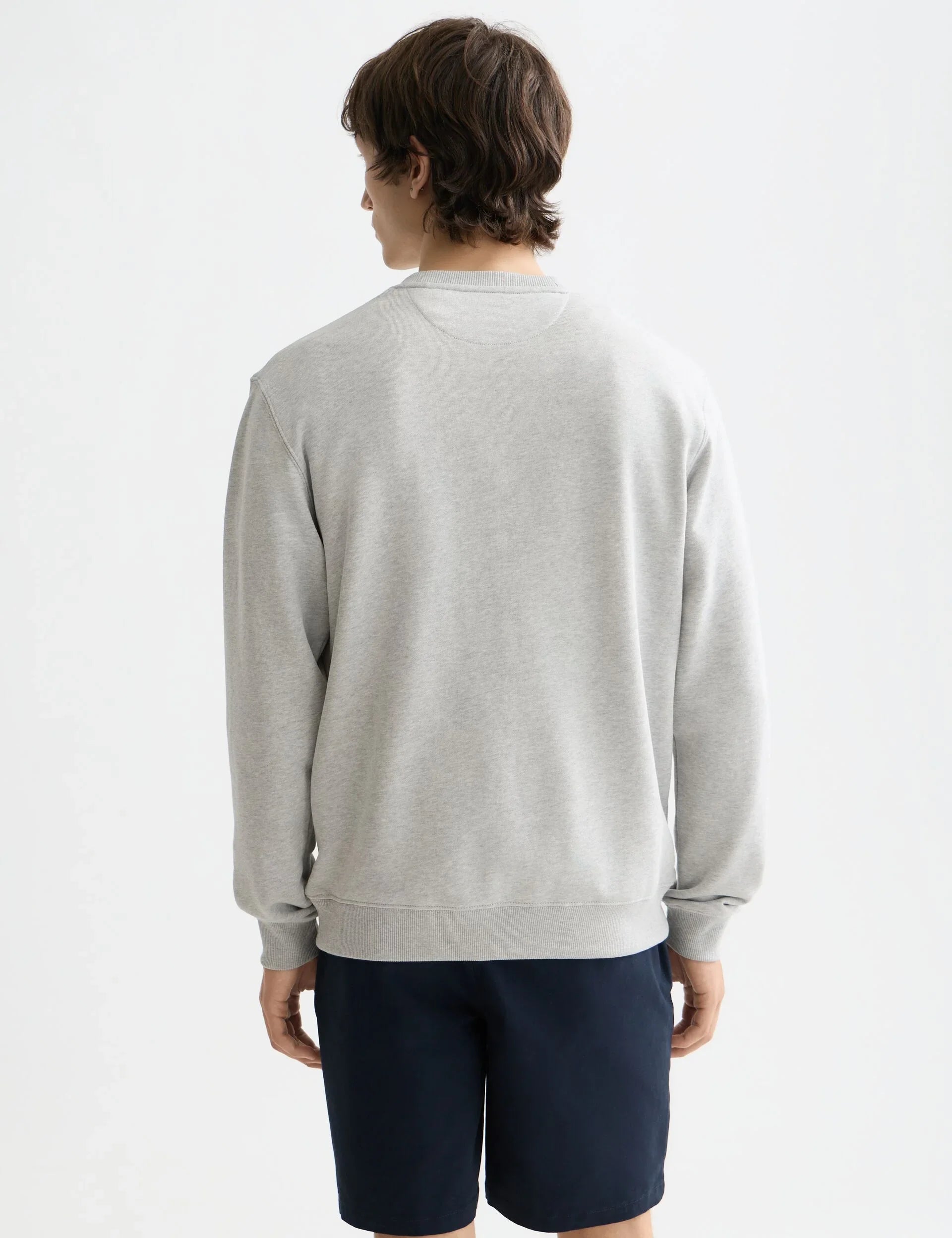 גבר בחולצת סווטשירט אפורה ומכנסיים קצרים כחולים, אופנה CHOZEN, צילום סטודיו