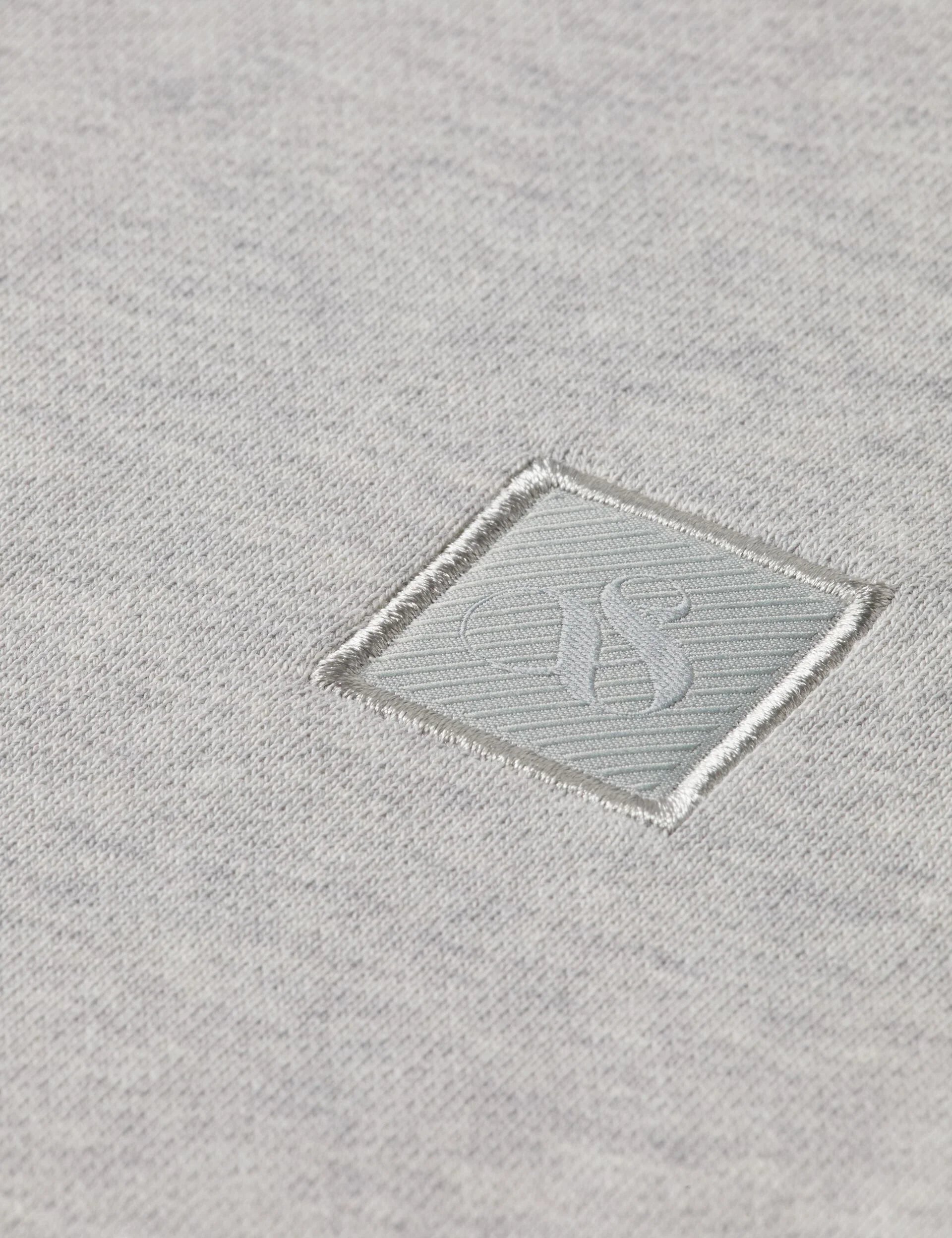 תקריב על בד אפור עם לוגו רקום בעיצוב יוקרתי, מותג אופנה CHOZEN מקבוצת אלפא