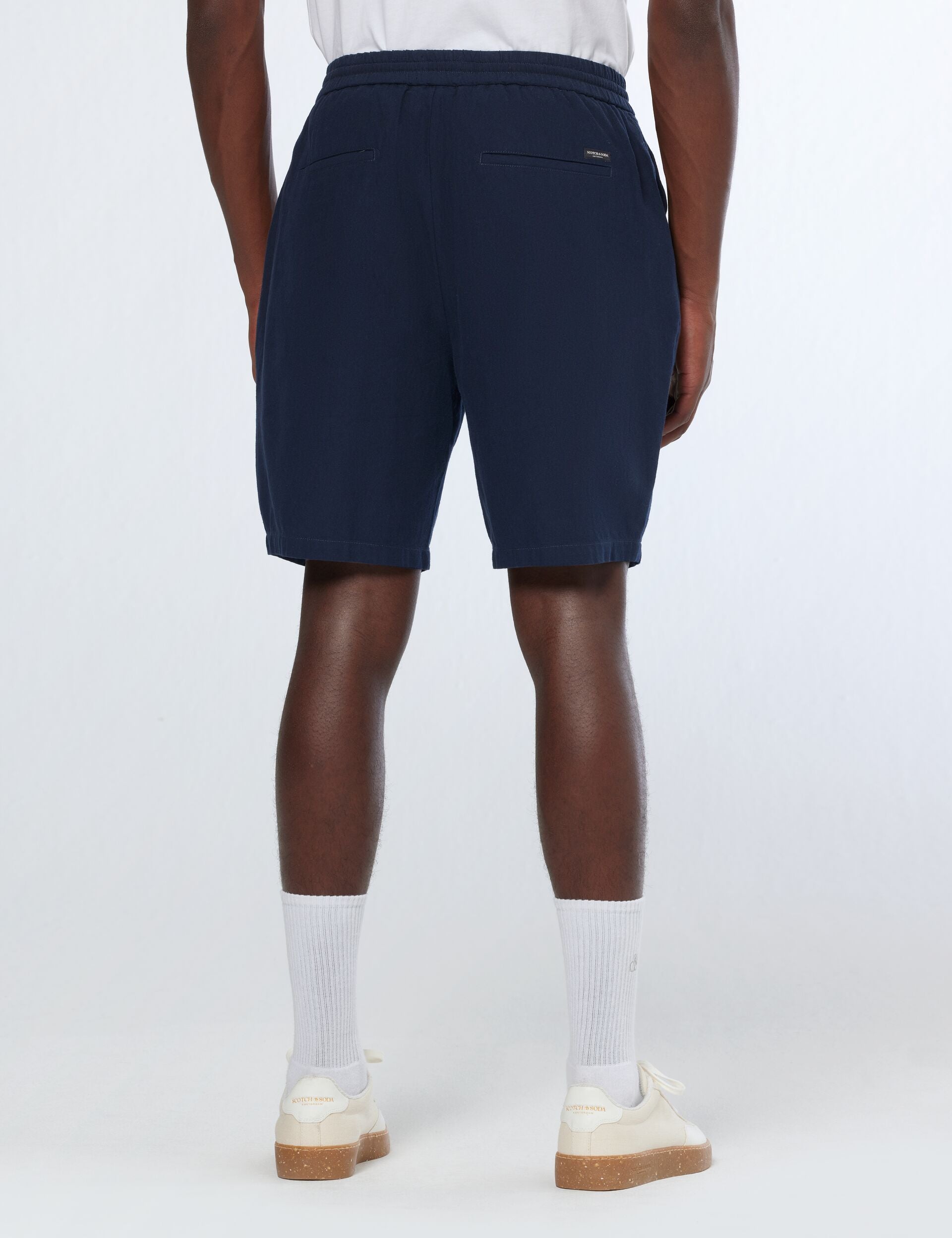 גבר לובש מכנסי ברמודה כחולים קצרים ונעלי סניקרס לבנות, אופנה מודרנית מ-CHOZEN