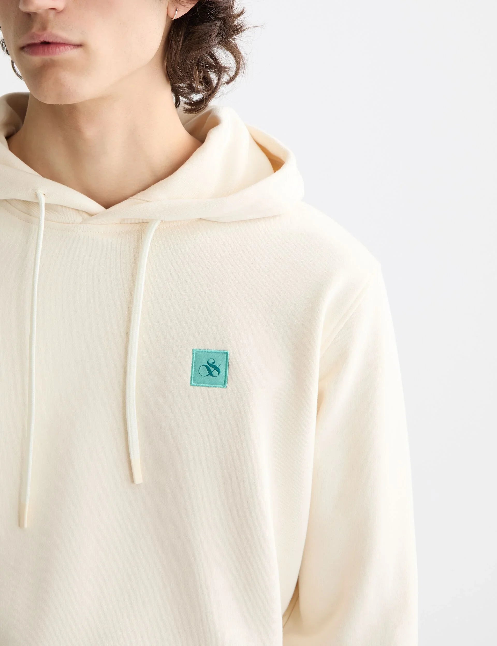 גבר לובש קפוצ'ון קרם עם לוגו קטן ירוק, CHOZEN מותגים מובילים