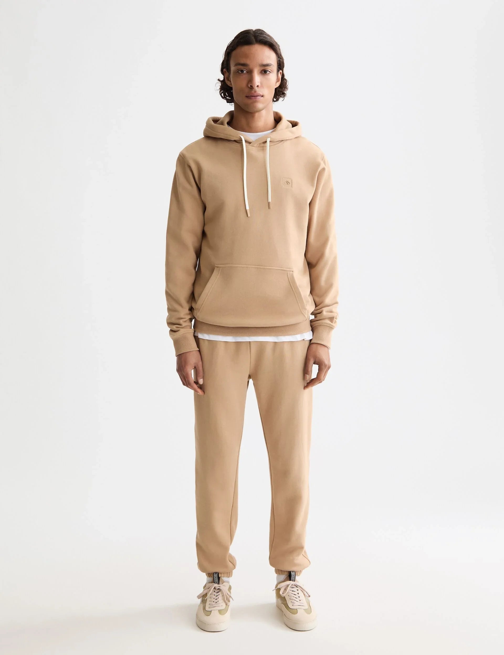 דוגמן לובש חליפת ספורט בצבע בז' עם קפוצ'ון ונעלי סניקרס, צילום לאתר CHOZEN