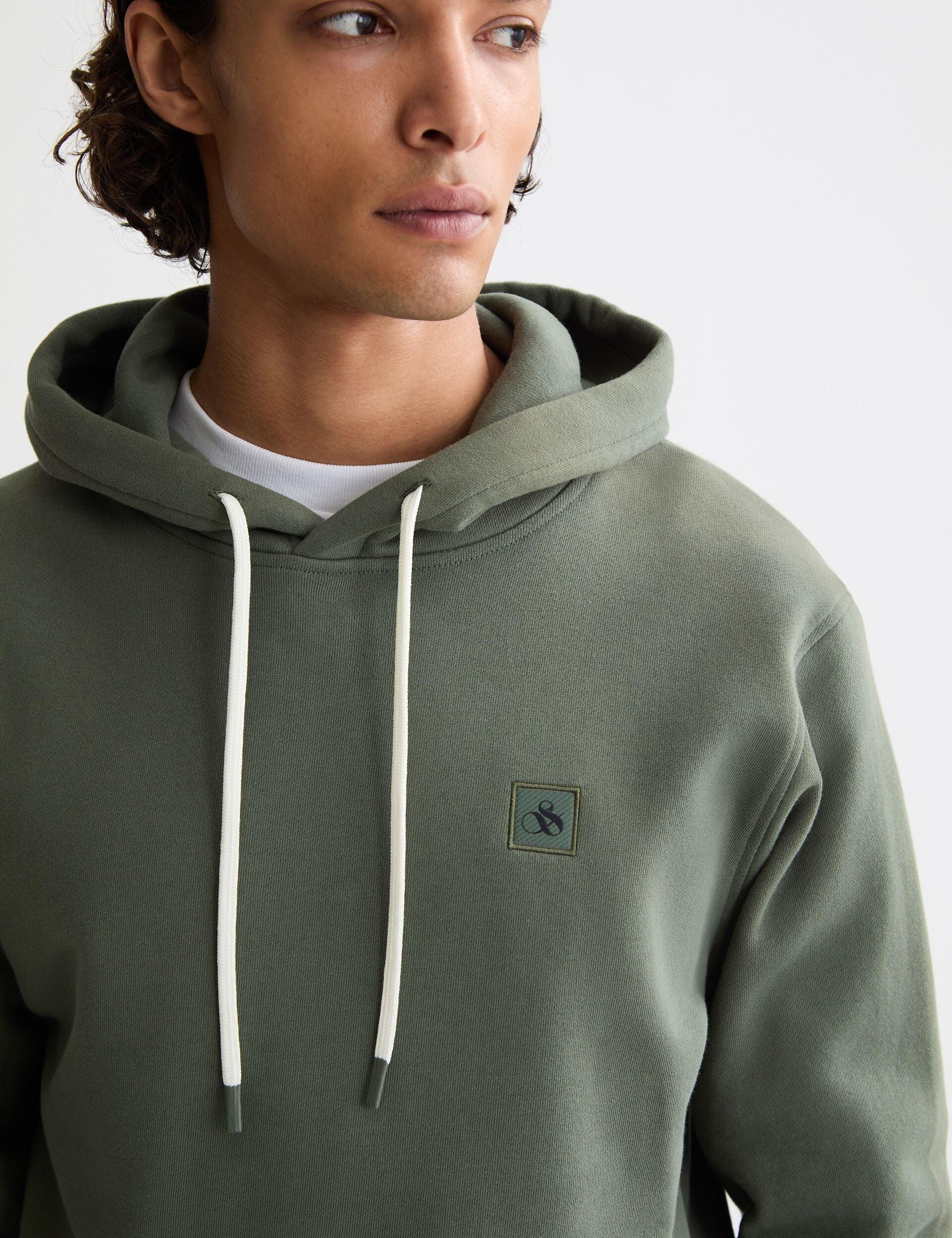 גבר לובש קפוצ׳ון ירוק עם שרוכים ולוגו קטן בחזית, אופנה לגברים CHOZEN