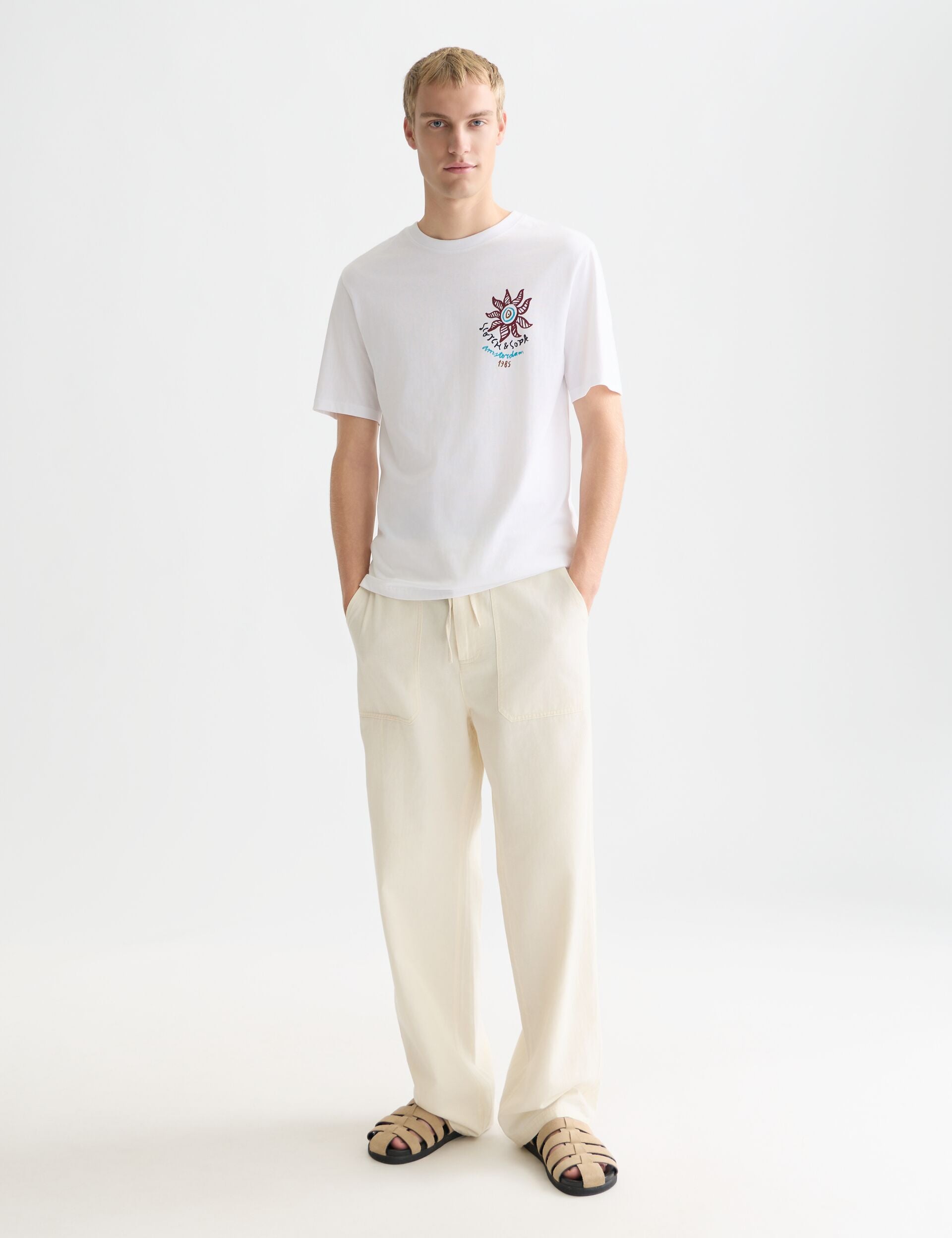 גבר לובש חולצת טי לבנה עם הדפס, מכנסיים בהירים וסנדלים, אופנת CHOZEN