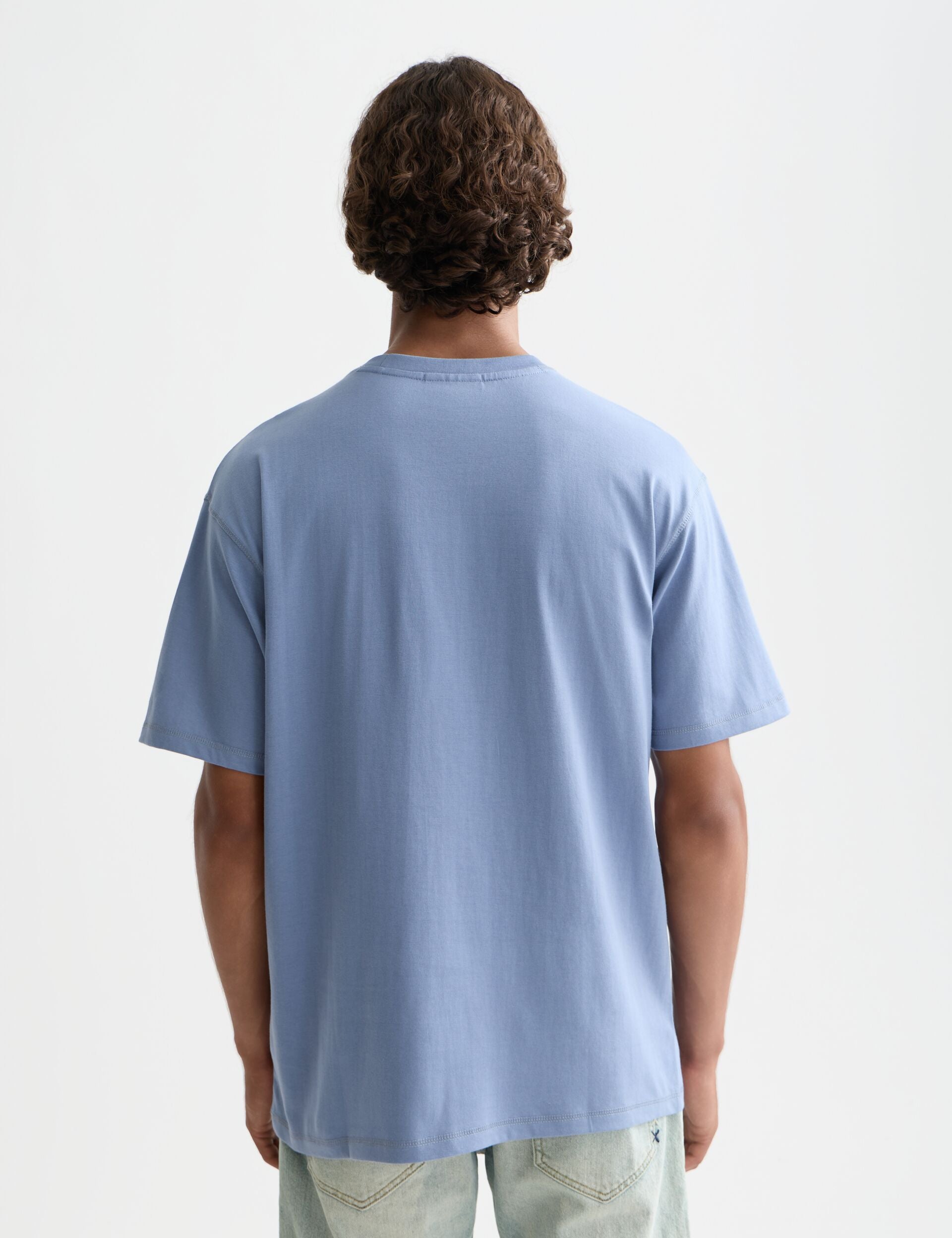 גבר עם שיער מתולתל לובש חולצת טי שירט כחולה ומכנסי ג'ינס בהירים, צילום גב, CHOZEN