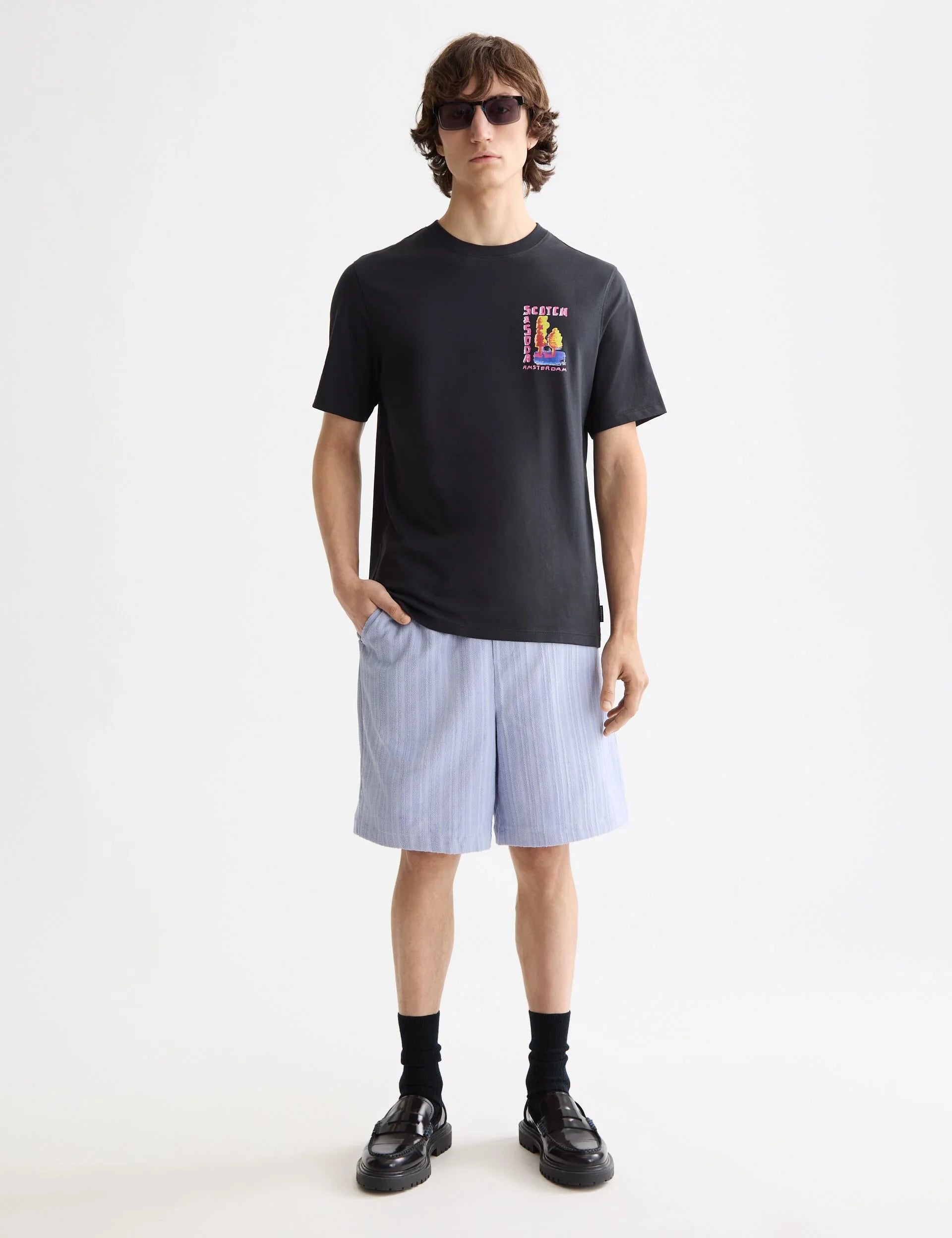 דוגמן לובש חולצת טי שחורה של Scotch & Soda ומכנסיים קצרים בהירים, אופנת גברים CHOZEN