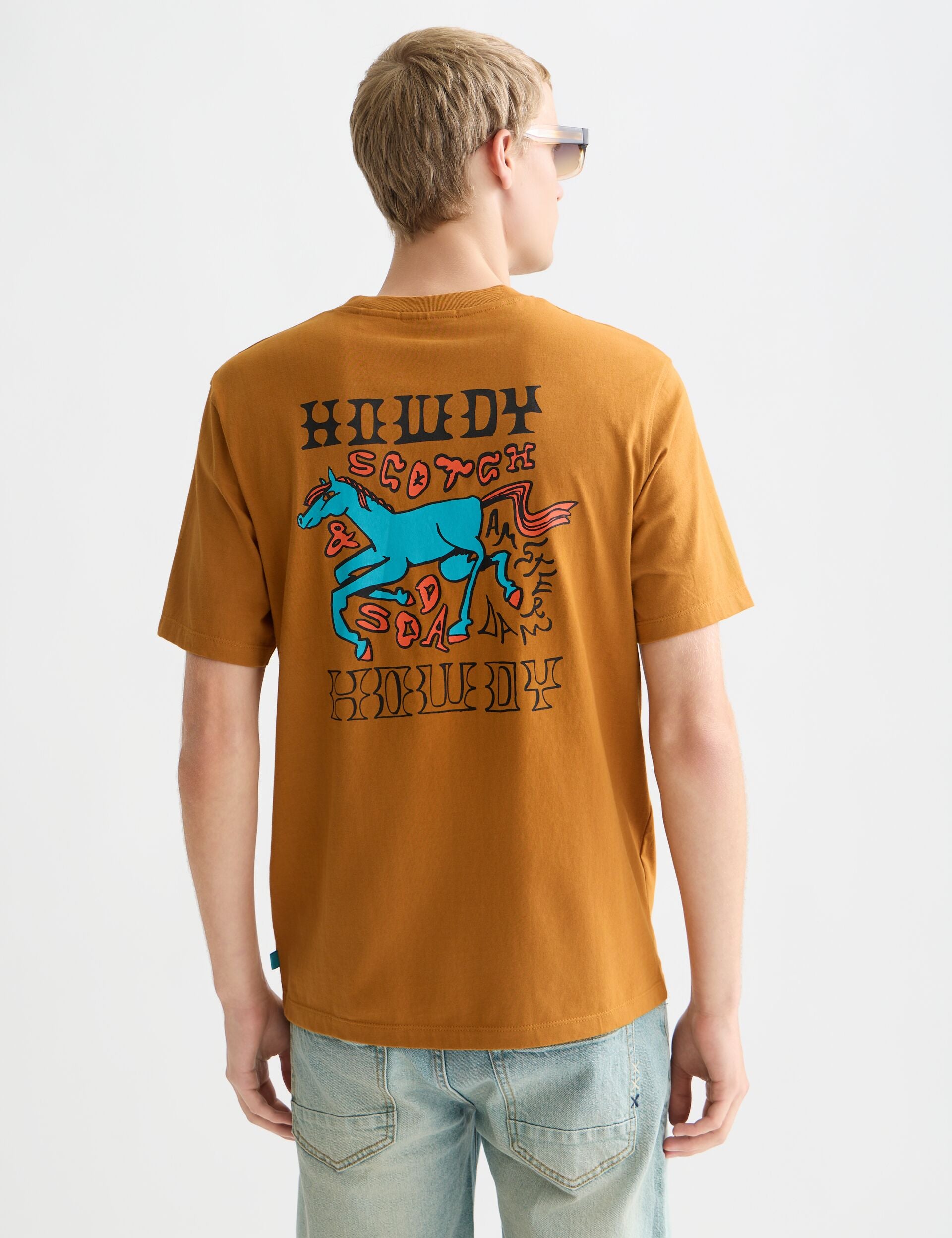 גבר עם חולצת טי חומה של CHOZEN, הדפס סוס כחול צבעוני בגב, ג'ינס, צילום אסתטי לאופנה