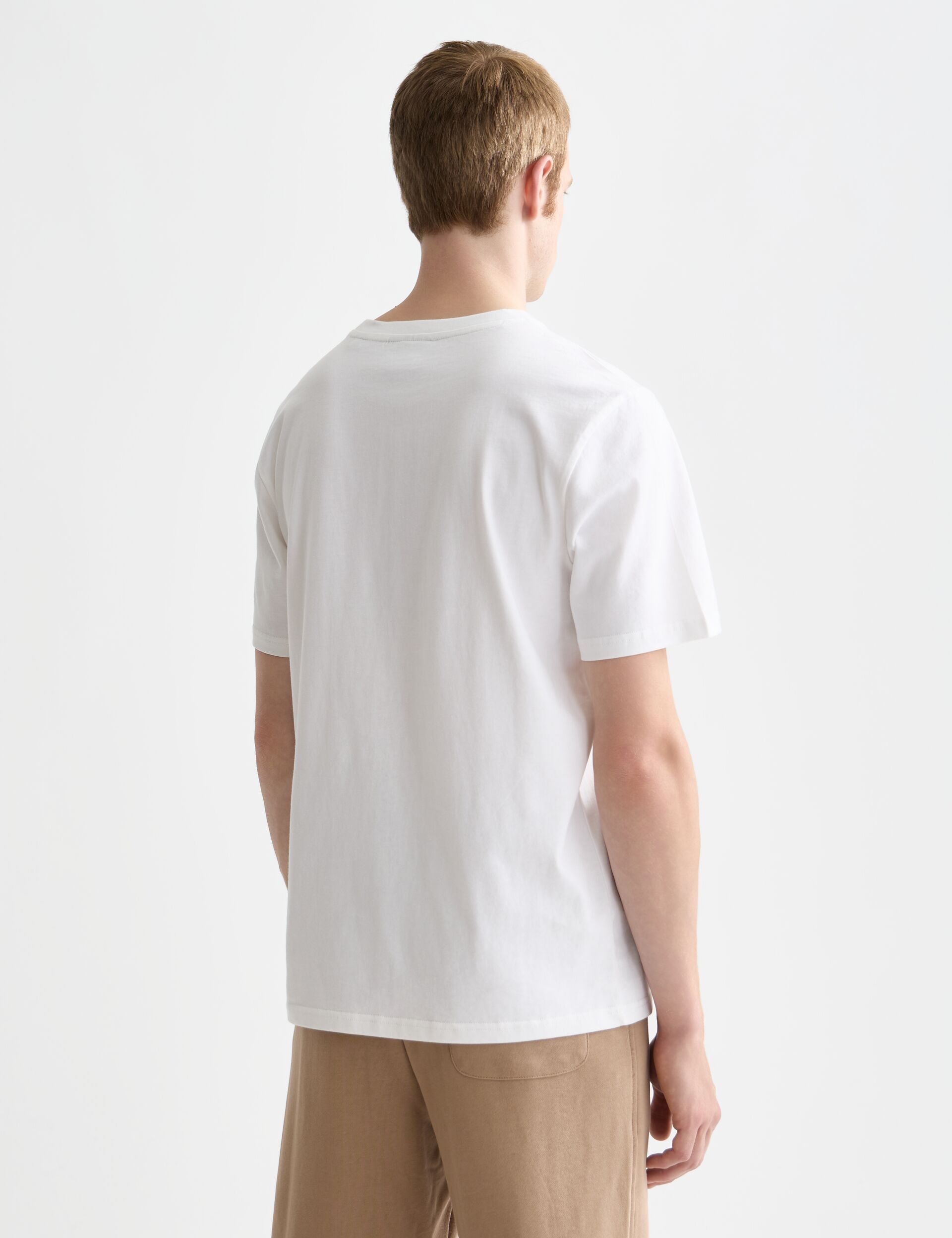 גבר עומד עם גב למצלמה, לובש חולצת טריקו לבנה ומכנסיים בגוון בז', רקע לבן, CHOZEN