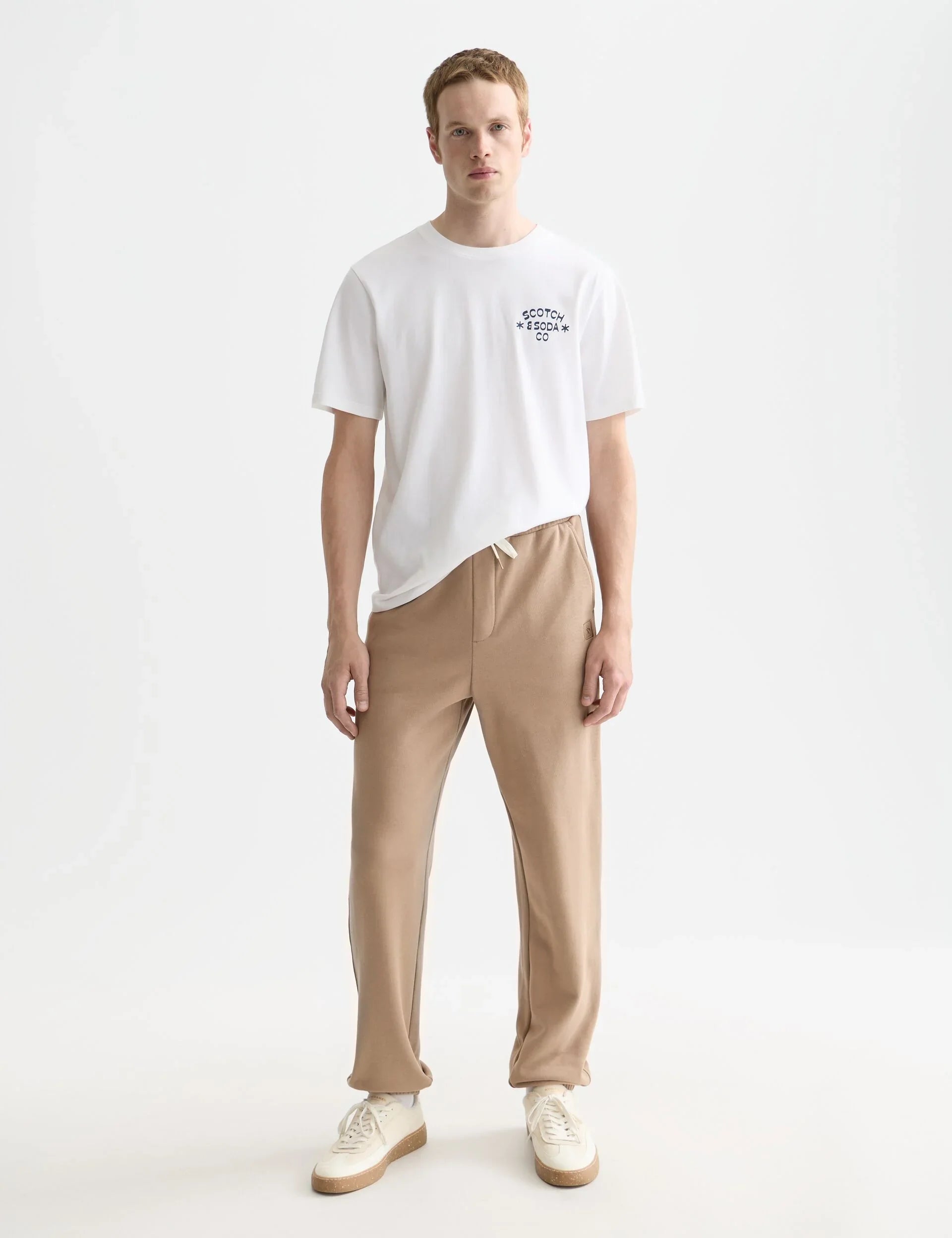גבר מדגמן חולצת טי לבנה של Scotch & Soda ומכנסיים בז' בסטייל קז'ואל, CHOZEN מותגים מובילים