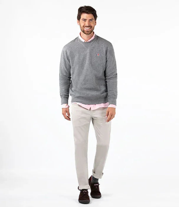 גבר לובש סוודר אפור CHOZEN עם חולצה ורודה, מכנסיים בהירים ונעליים כהות על רקע לבן