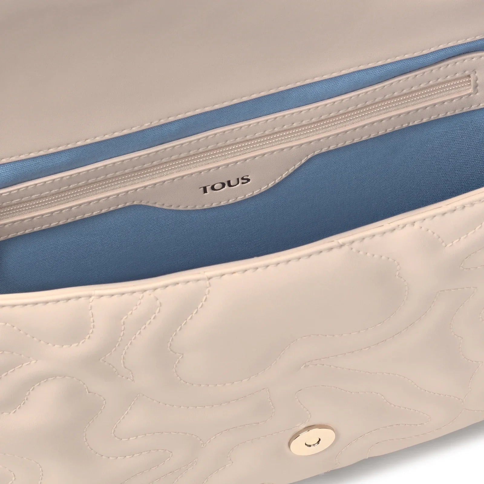 תקריב של תיק TOUS בעיצוב קרם עם ריפוד כחול, תיק אופנתי ממותג ב-CHOZEN